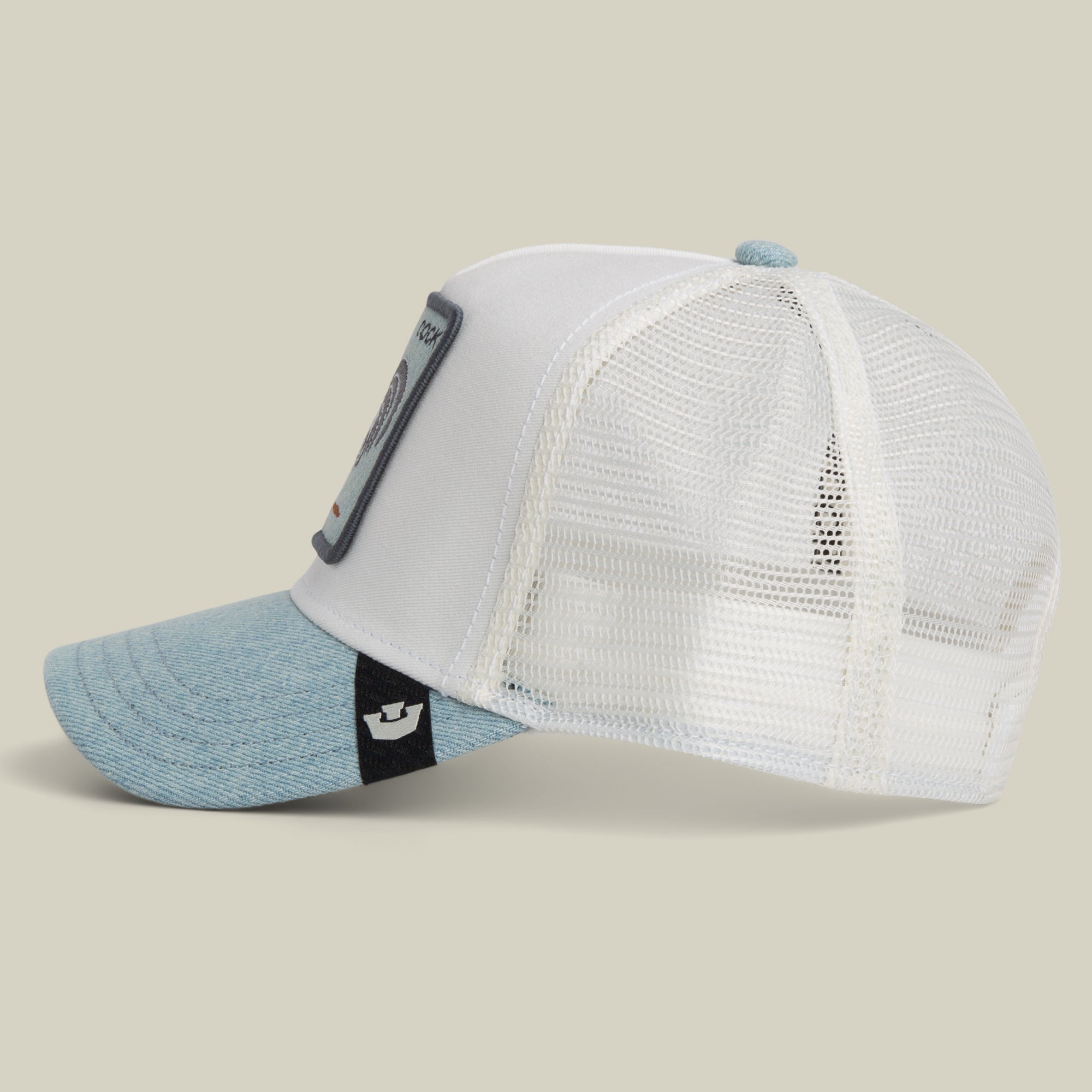 The Denim Rooster by Goorin Bros. is a white mesh-back baseball cap featuring a light blue brim and a rectangular rooster patch on the front. Shown in side profile against a plain background, this trucker hat highlights its distinctive design.