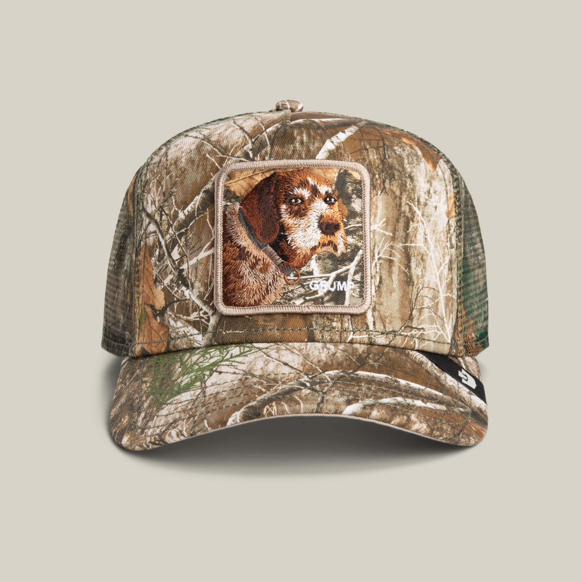 The Goorin Bros. Realtree Edge Grump Dog cap features a camouflage color, breathable mesh back, and a front patch embroidered with a brown dog.