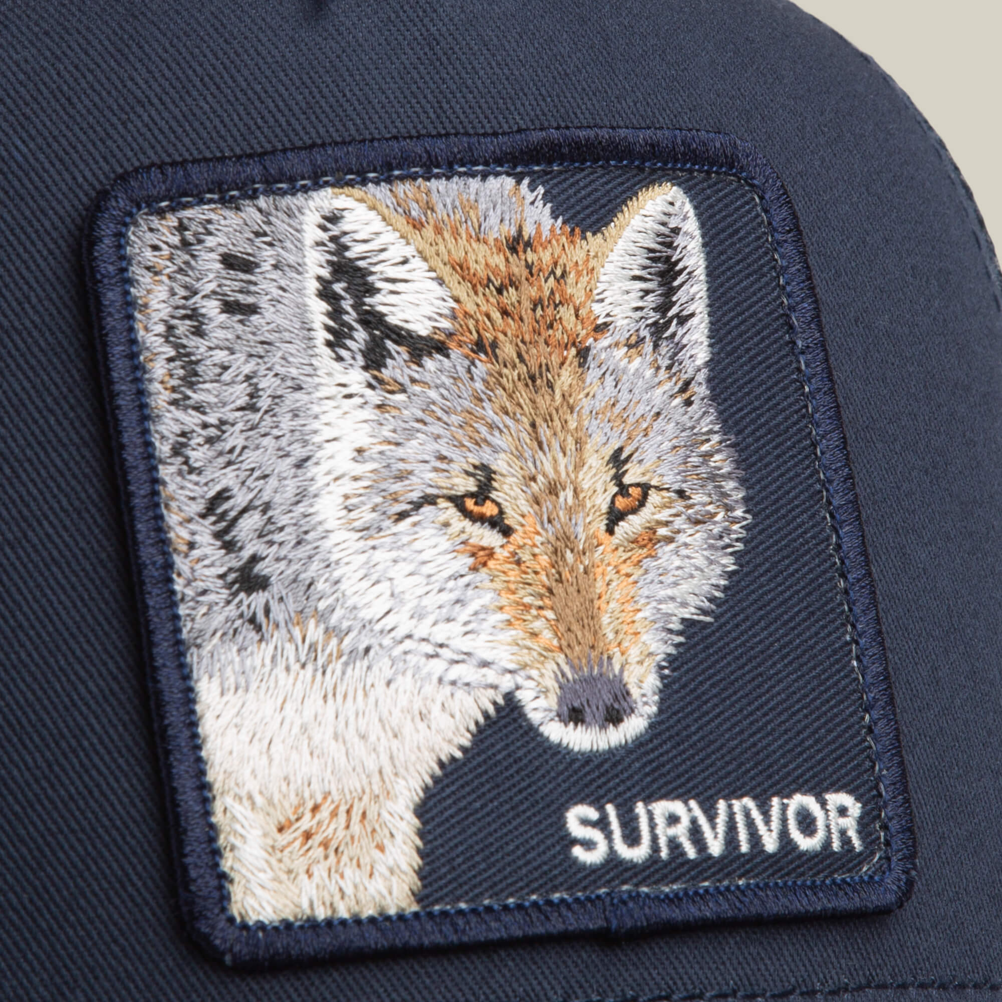 A close-up of the Goorin Bros. Mirage Survivor navy trucker hat, featuring a fox face patch and SURVIVOR embroidered below.