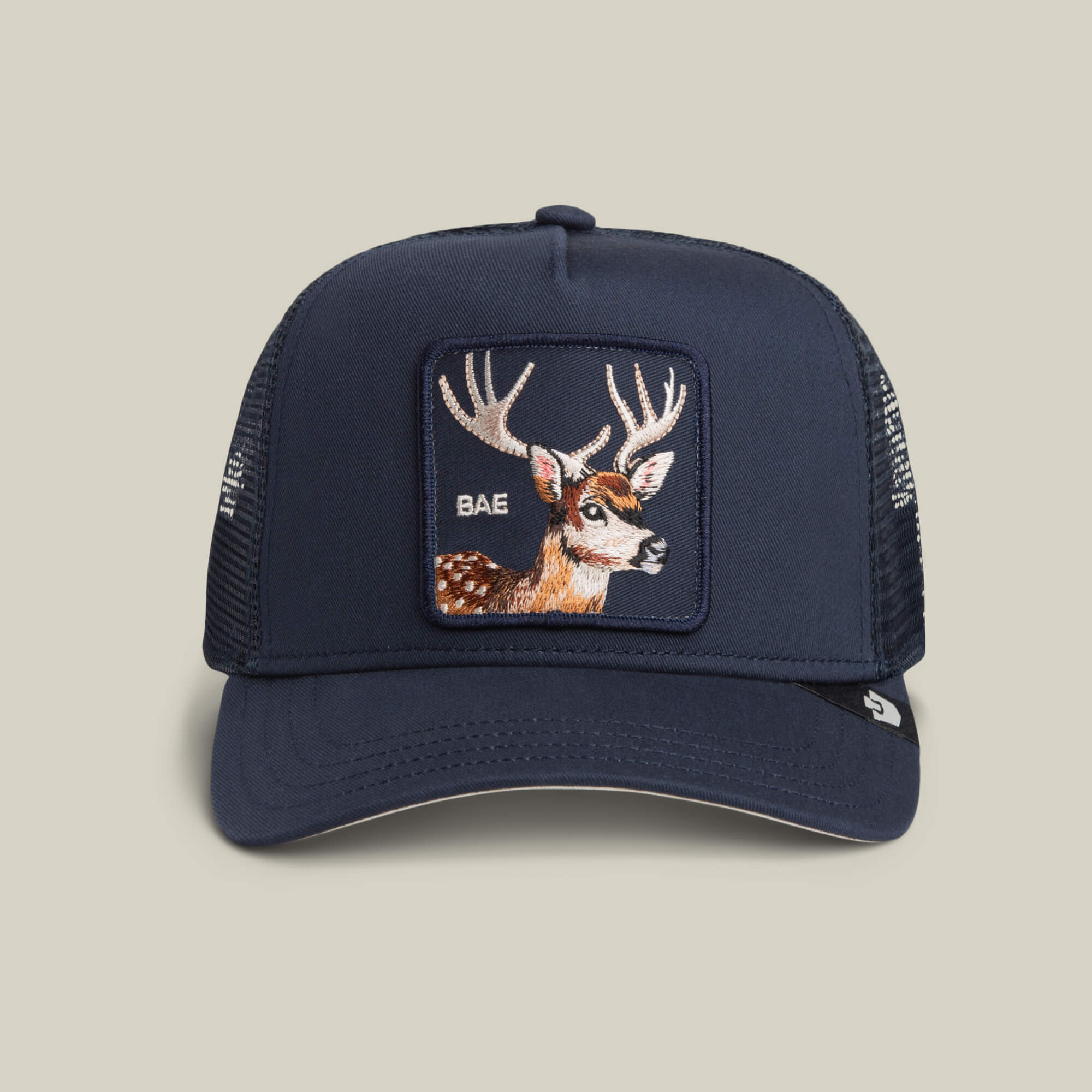 The Goorin Bros. Mirage Bae hat in EDGE features a mesh trucker design and front deer patch embroidered with "BAE" on a light tan background.
