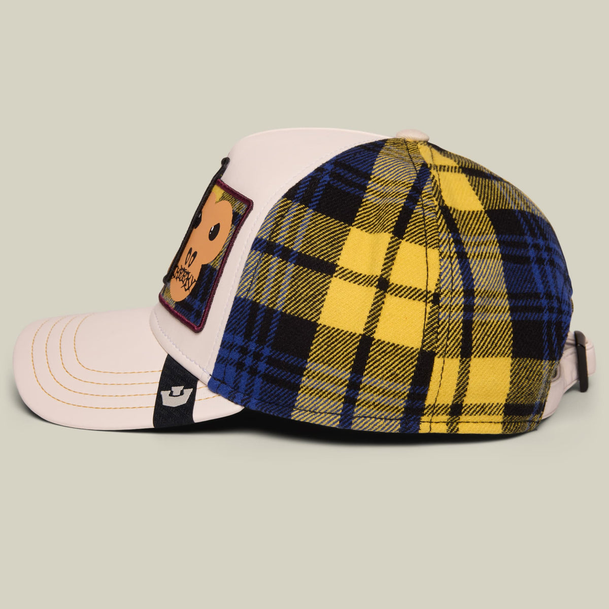 The Goorin Bros. Cheeky baseball cap features a color-blocked design with a cream and white front panel, navy and yellow tartan plaid back, and a decorative patch on the side, shown on a neutral background.