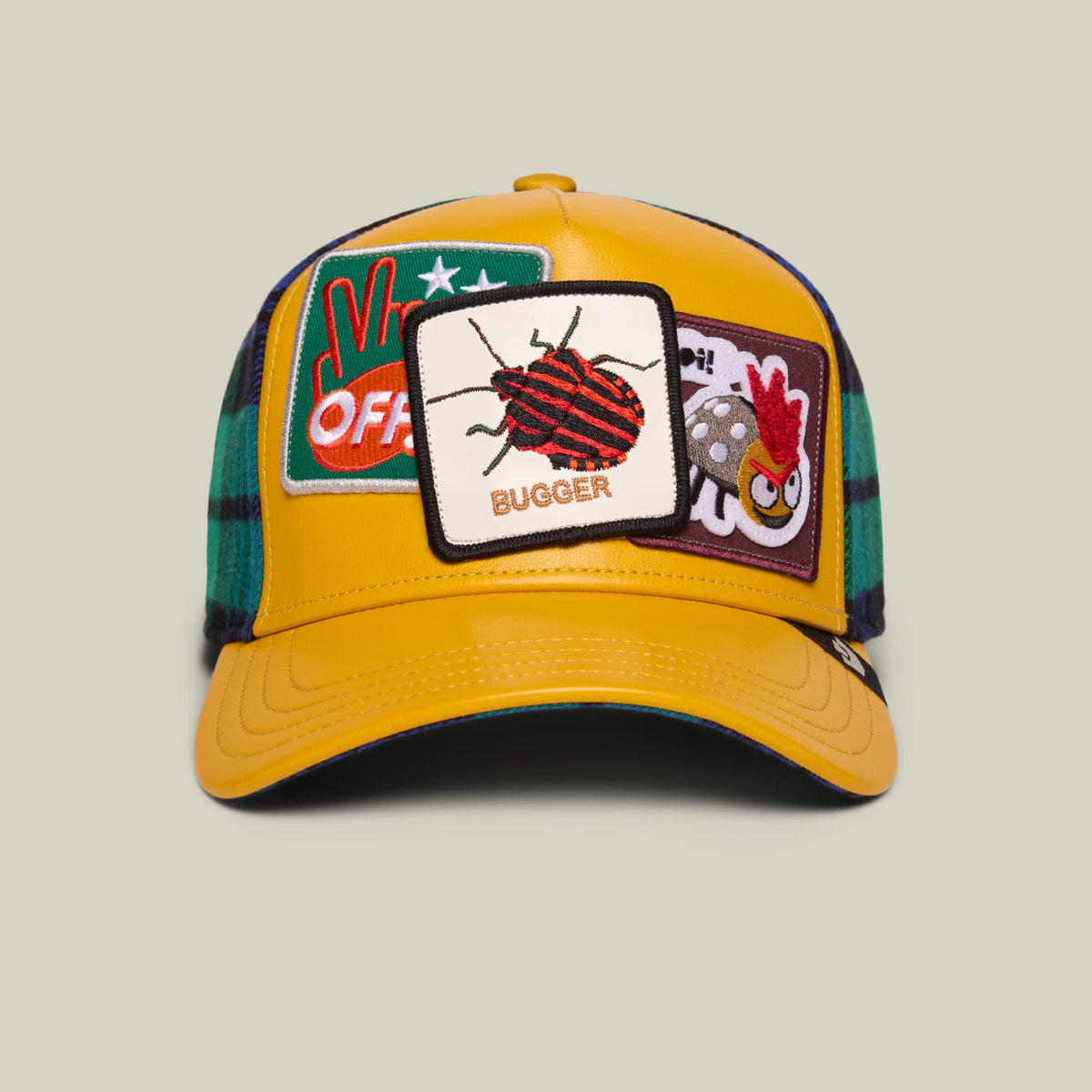 The Goorin Bros. Bugger trucker hat features a yellow front panel with colorblock navy and green sides, adorned with embroidered patches including a red striped beetle design and colorful graphics, displayed against a neutral background.