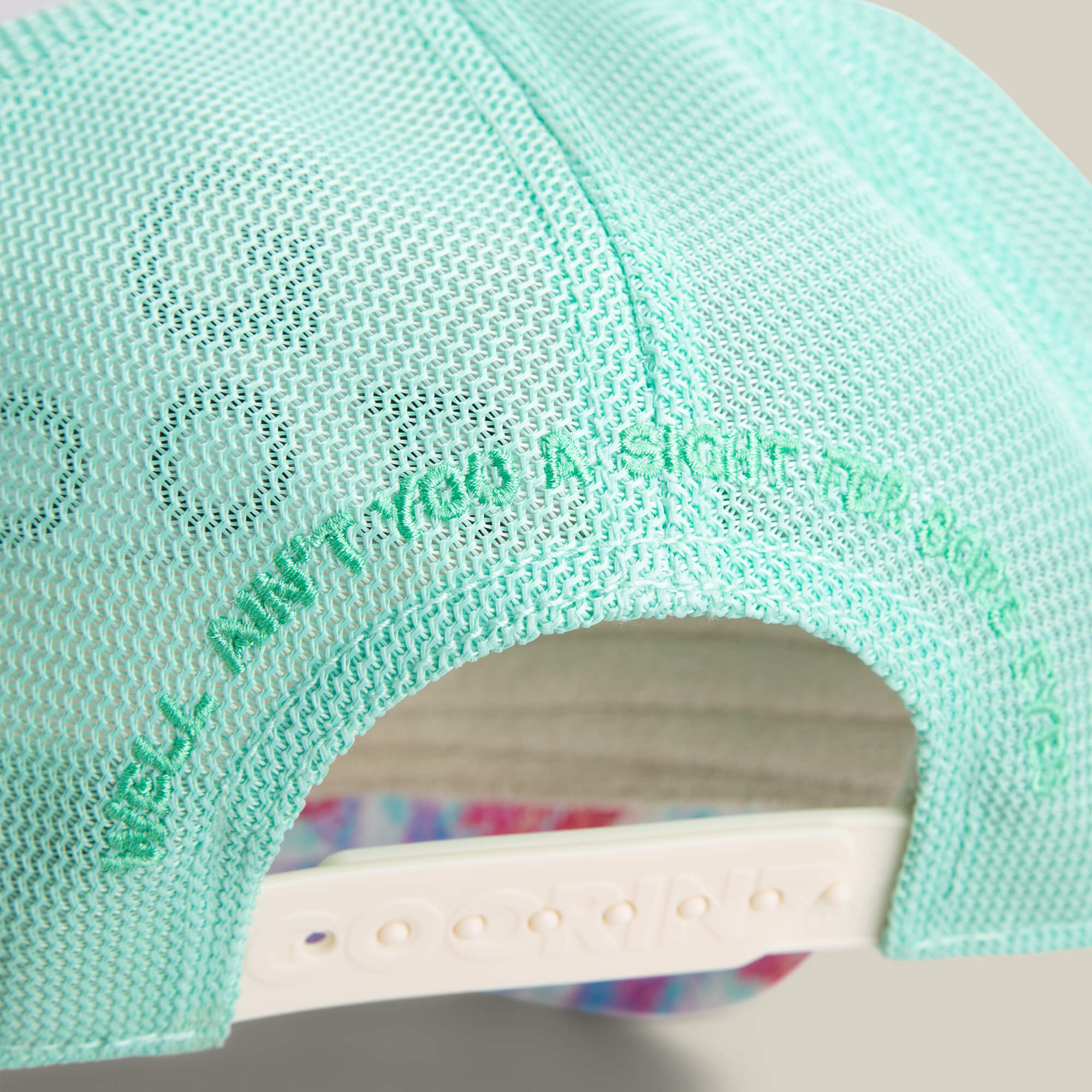 Close-up of the back of the Goorin Bros. Magic Eye hat, featuring light blue mesh, green embroidered text, and a white adjustable strap for a subtle mirage effect with its unique design.