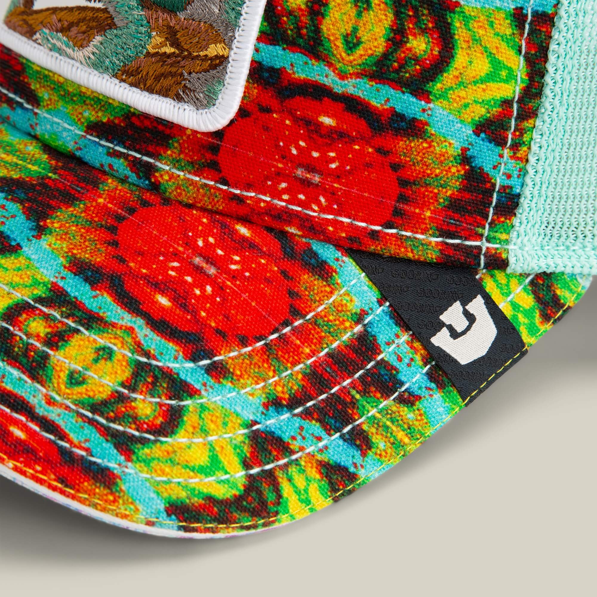 Close-up of the Goorin Bros. Magic Eye cap, featuring a vibrant red, green, and blue abstract pattern reminiscent of optical illusions, mesh fabric, and a black tag with a white geometric logo.