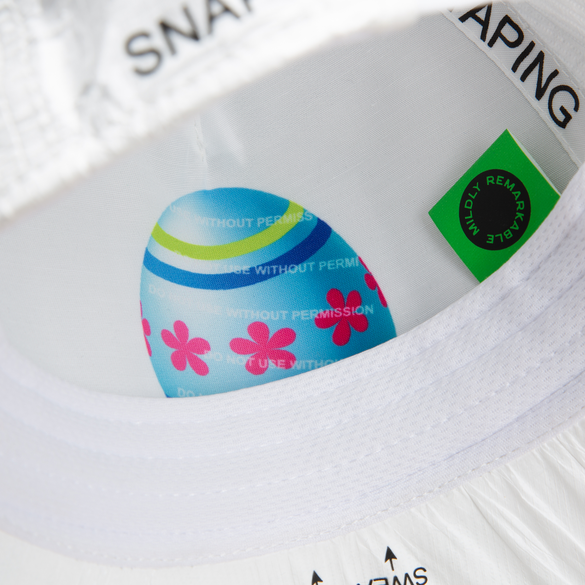 A close-up of the inside of the limited edition K.I.S.S. white hat by Goorin Bros. shows a colorful egg with pink flowers, blue stripes, a green label, and black printed text.