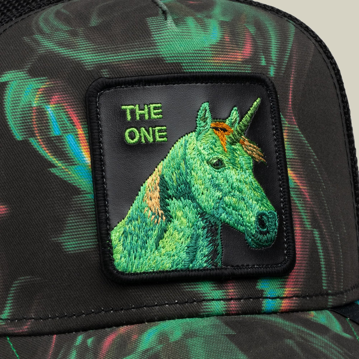 The Goorin Bros. No Spoon trucker hat features an embroidered green unicorn patch with gold accents on a black fabric base with colorful psychedelic patterns throughout.