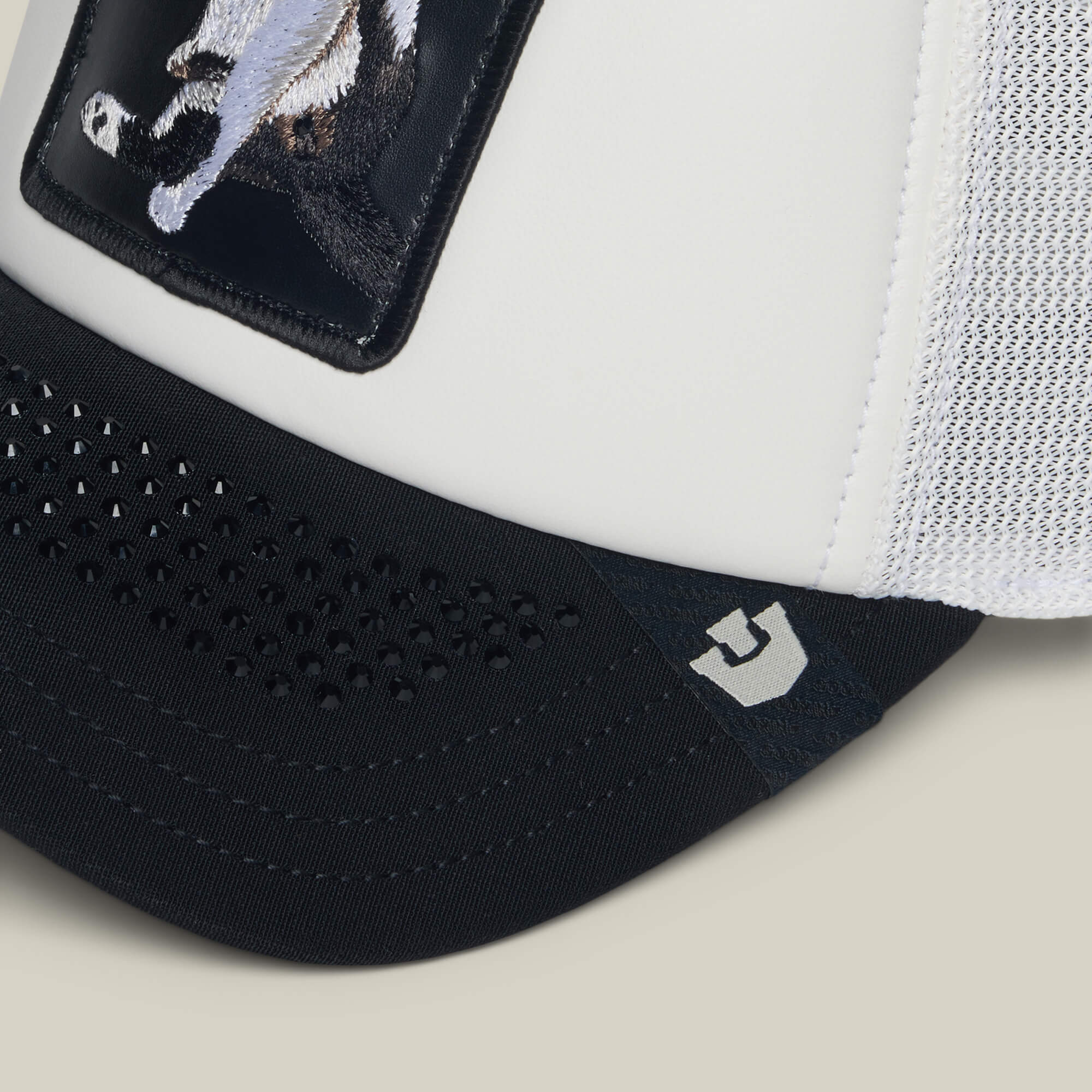 Close-up of the Goorin Bros. "R U Done Eating?" white trucker hat featuring a black brim, mesh side panel, animal patch on the front, and a small gray logo—ideal for adding a polite vibe to casual settings.
