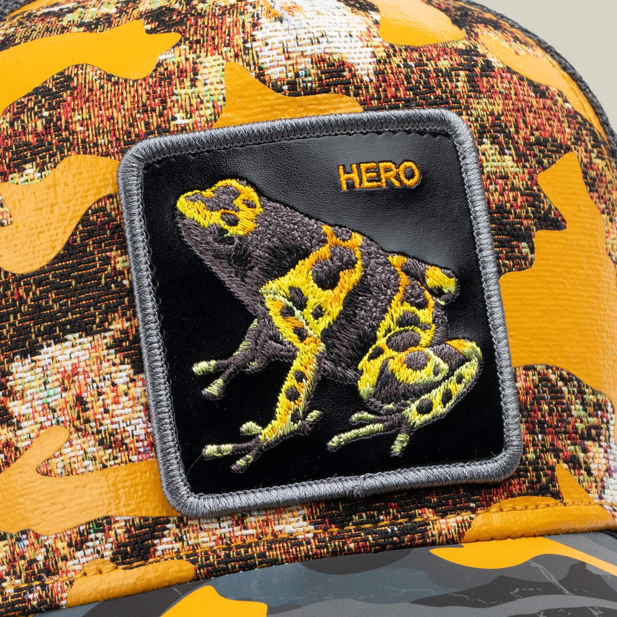 The Goorin Bros. "Knight in Sliming Armor" is a golden camo trucker hat with a yellow and black frog Hero patch featuring "HERO" boldly stitched, inspired by the Yellow Swamp Battalion.