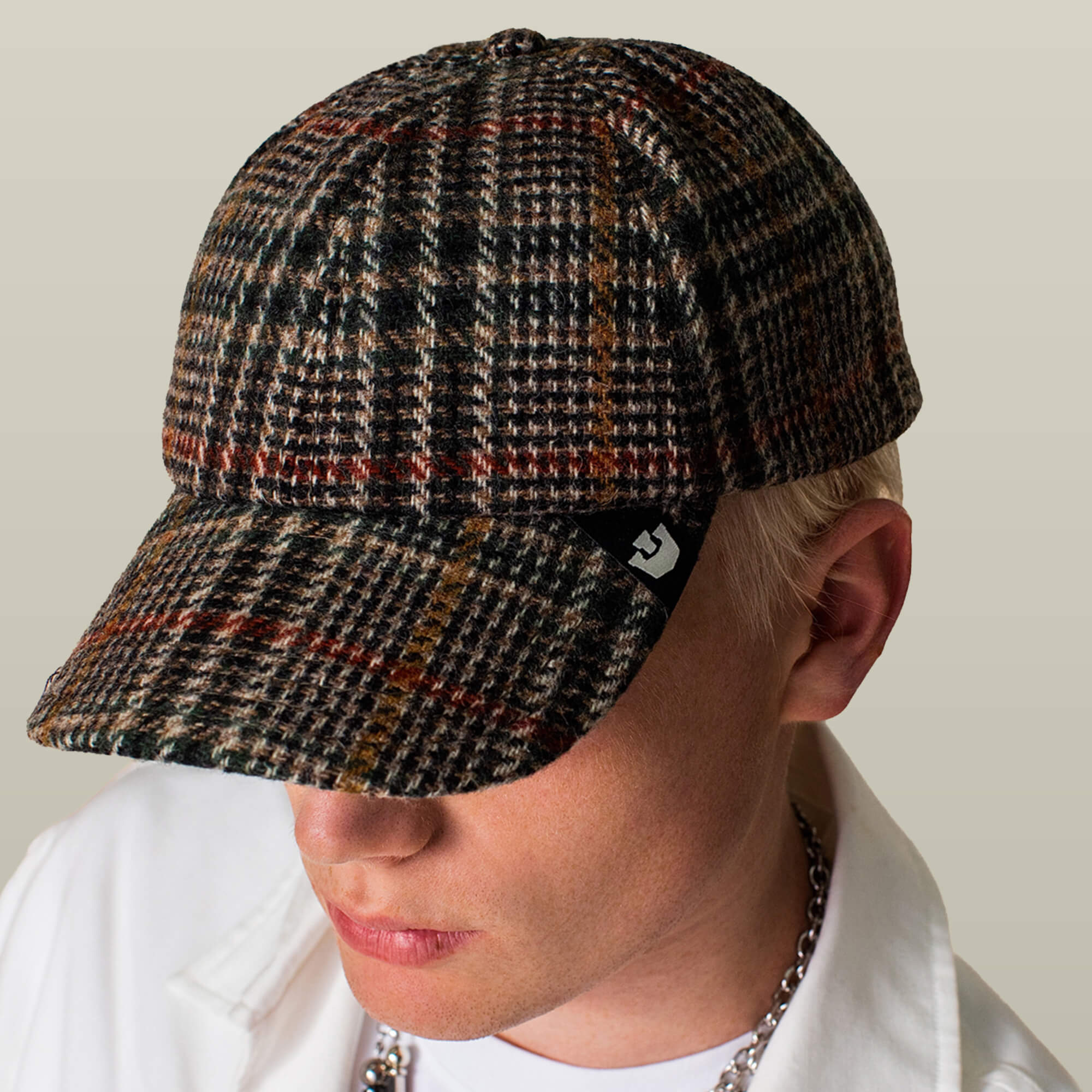 A person wearing the Goorin Bros. Cozy Tailored Baseball cap, a six-panel plaid design with a curved brim, and a white collared shirt looks downward against a plain background.