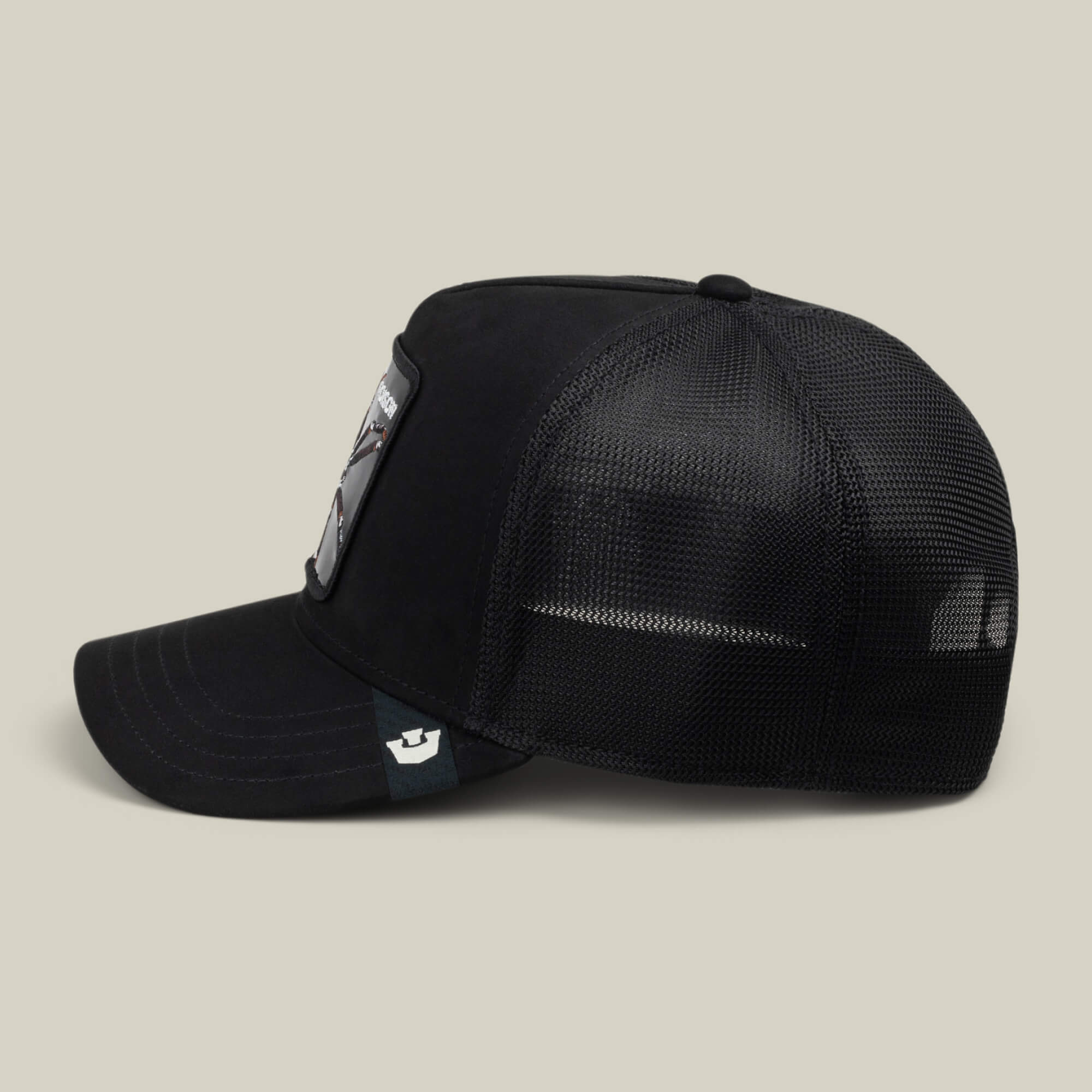 Black Out Spider hat by Goorin Bros. shown in side profile on a plain background, featuring a rectangular collectible spider patch trucker design on the front and a small tag on the side of the visor.