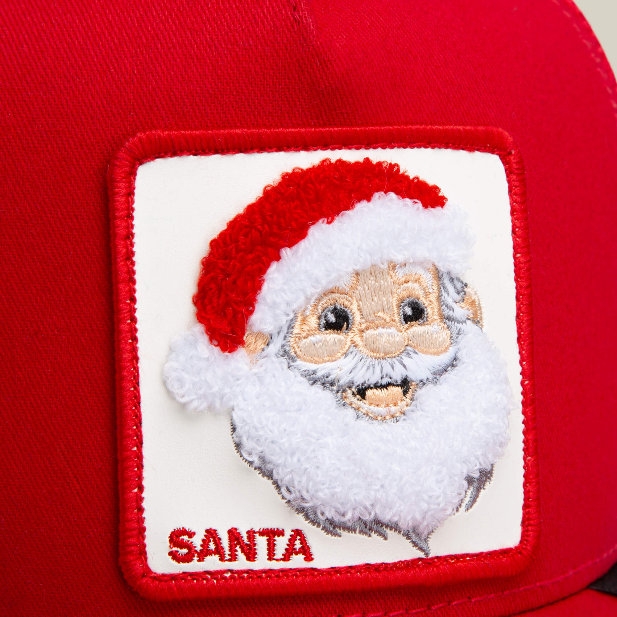 Close-up of the Goorin Bros. "Mr. Claus" red Santa hat, featuring a patch with an embroidered Santa face and “SANTA” stitched below—perfect for holiday celebrations.