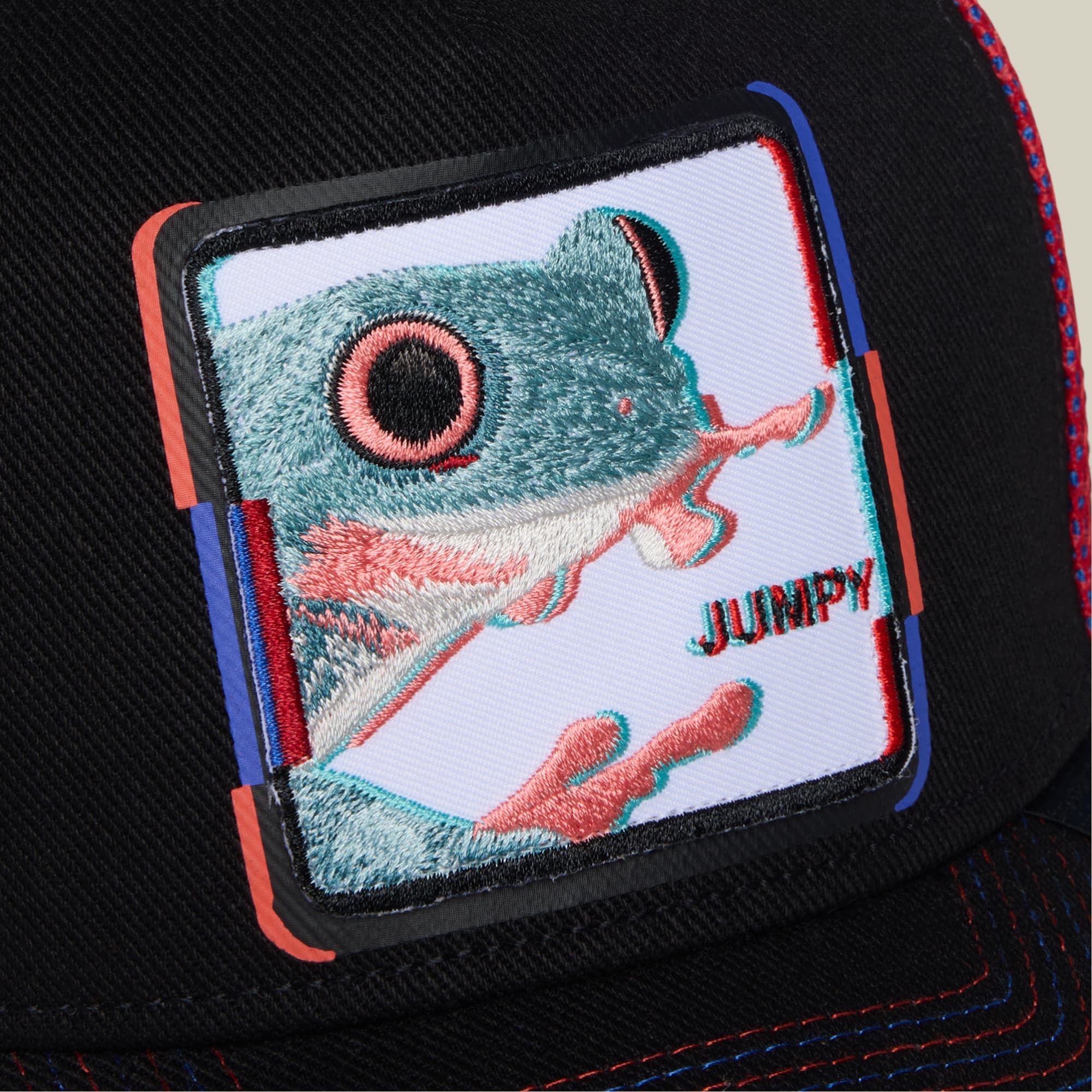 The Goorin Bros. Bug Fixes trucker hat features a black snapback with a colorful embroidered patch depicting a turquoise frog with coral accents and the word Jumpy on a light background, accented with red and blue trim.