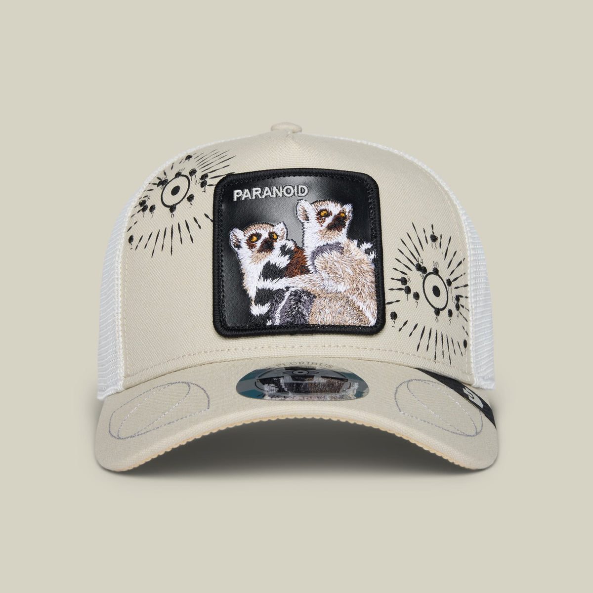 The G-Anon by Goorin Bros. is a beige and white trucker hat featuring a black embroidered patch of meerkats with the word Paranoid, decorative sun designs on the sides, and mesh back panels.