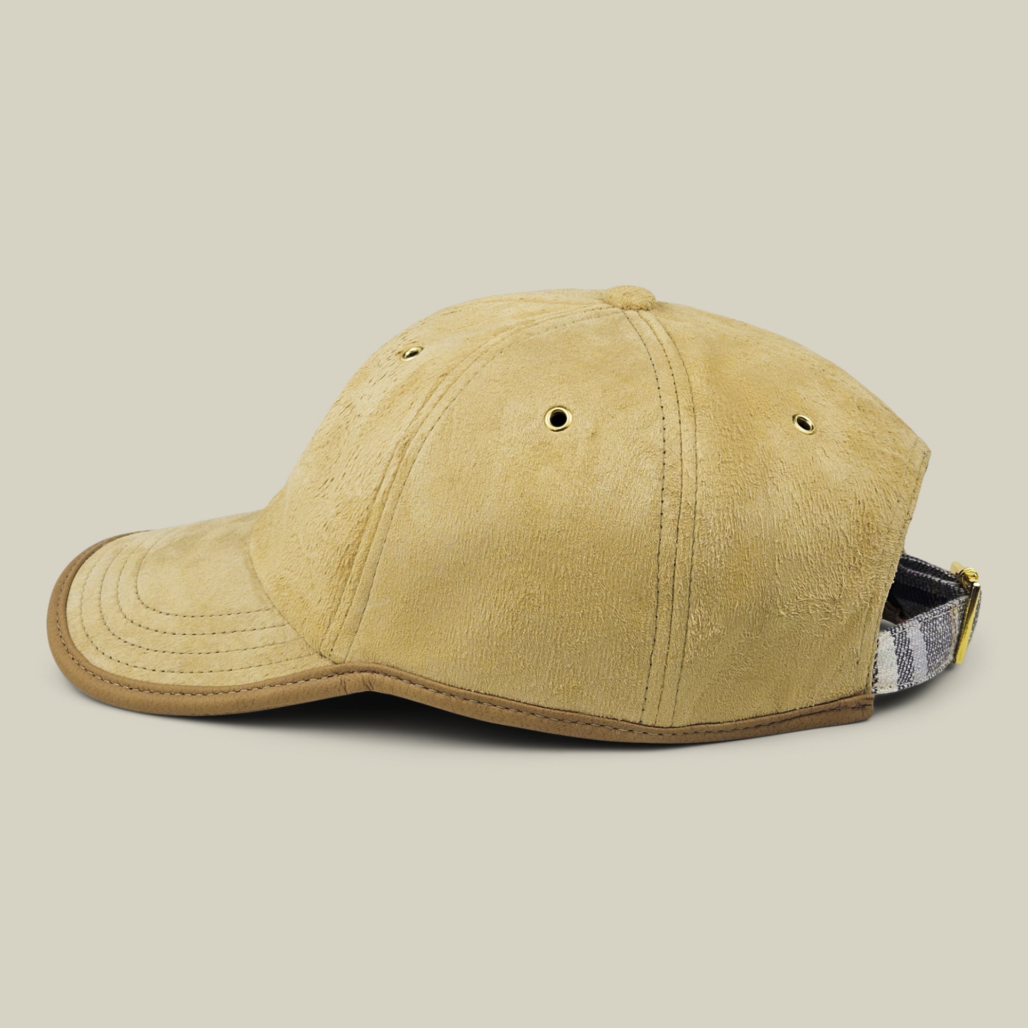 The Steiner papa cap by Goorin Bros. in tan suede is shown in profile, featuring ventilation eyelets, a curved brim, and an adjustable plaid strap accent at the back.