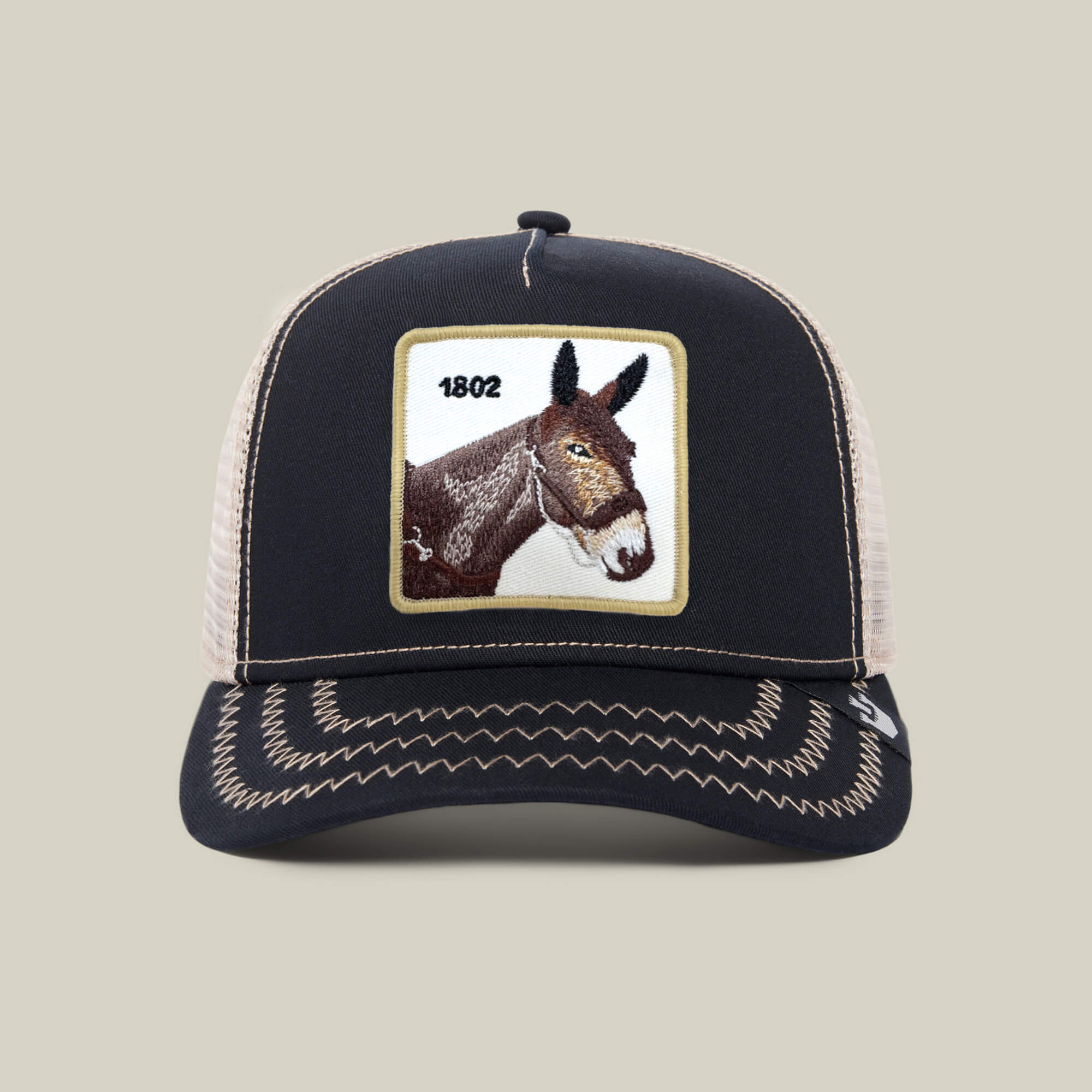 The Goorin Bros. 1802 Mule trucker hat features a black front with an embroidered mule’s head and “1802,” plus a beige mesh back.