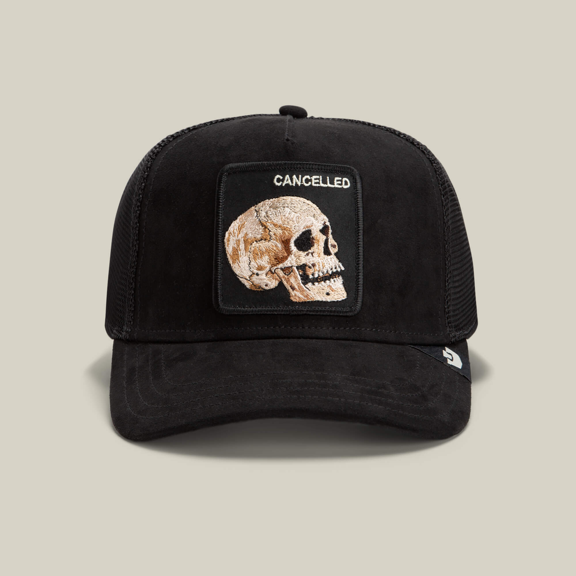 The Bold Suede Skull by Goorin Bros. in Void Black features a stitched skull and bold "CANCELLED" patch, delivering classic trucker hat style with an edgy twist against a light background.