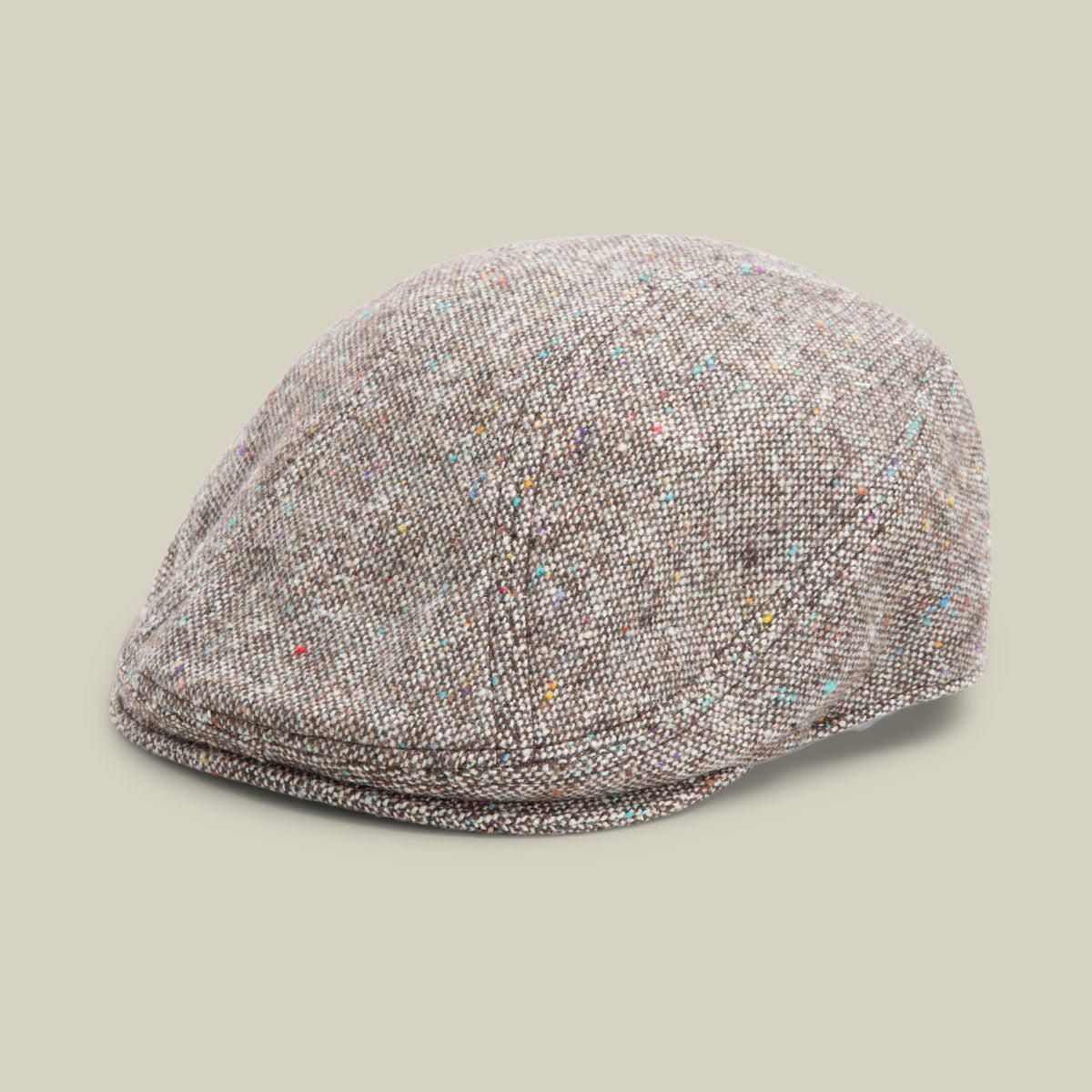 A Goorin Bros. Gibbins flat cap in the color GROUND, featuring a speckled tweed pattern inspired by classic men’s styles, displayed against a plain beige background.