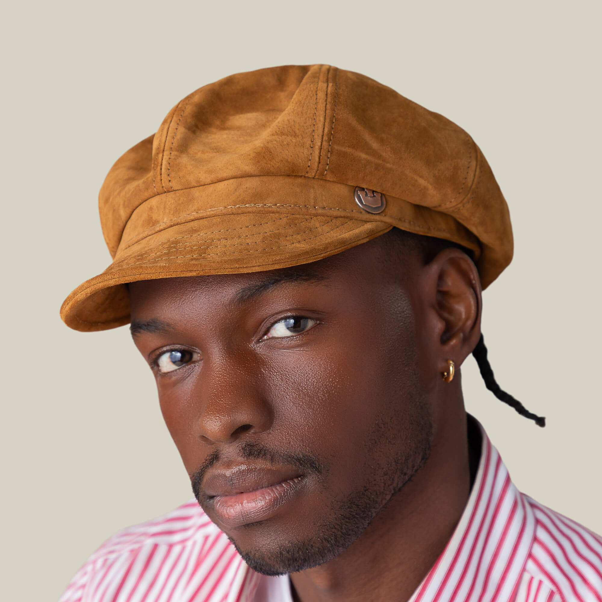 A person wearing the Goorin Bros. Ruthy suede cabbie flatcap, a red and white striped shirt, and a gold hoop earring poses against a plain beige background.