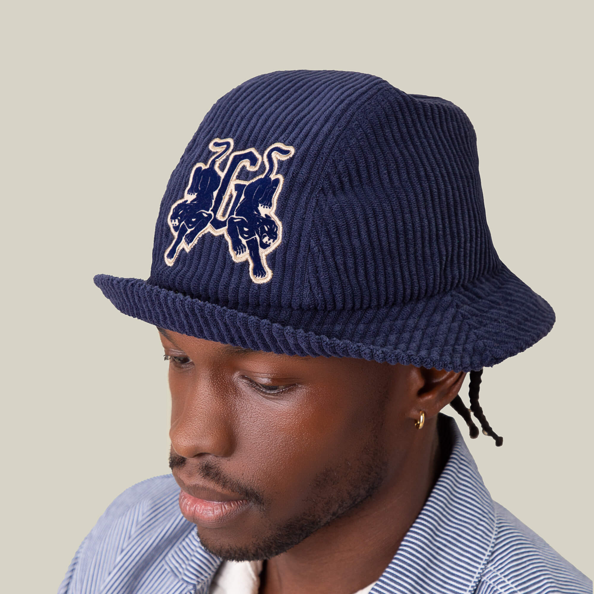 A man wears the Goorin Bros. "Yes Coach" navy ribs corduroy bucket hat with an embroidered front graphic and a striped button-up shirt, set against a plain background.
