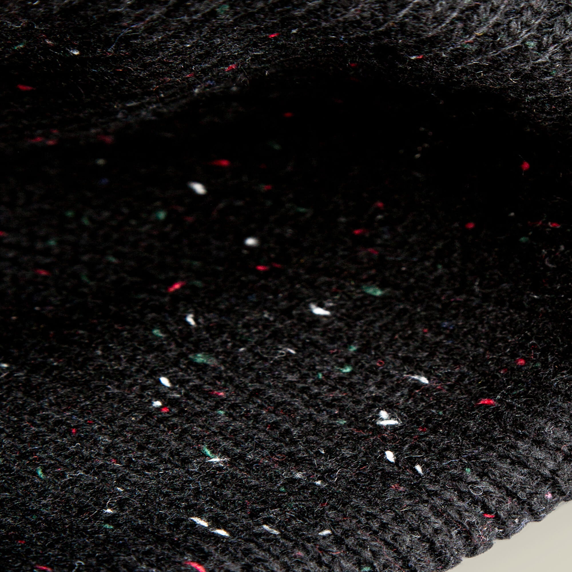 Close-up of the Goorin Bros. No Comply beanie, featuring black knit fabric with subtle white, red, and green flecks woven throughout its warm material.