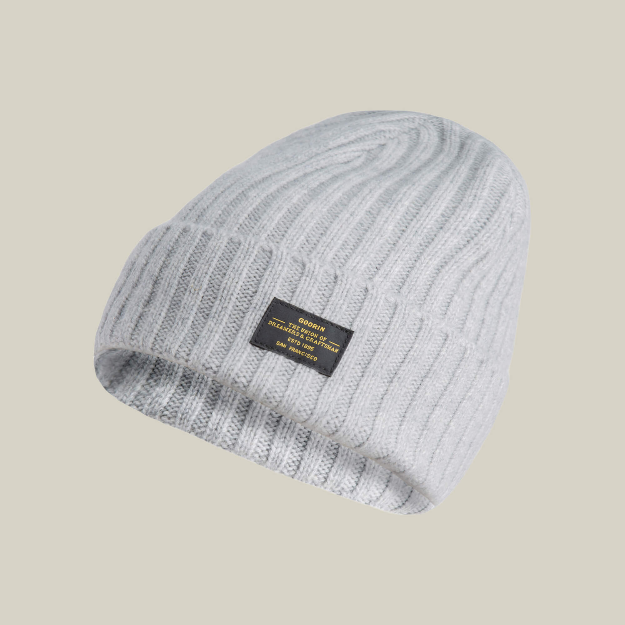 The Goorin Bros. Dream Cap is a light gray luxurious knitted beanie with a black rectangular label on the front, featuring yellow and white text.