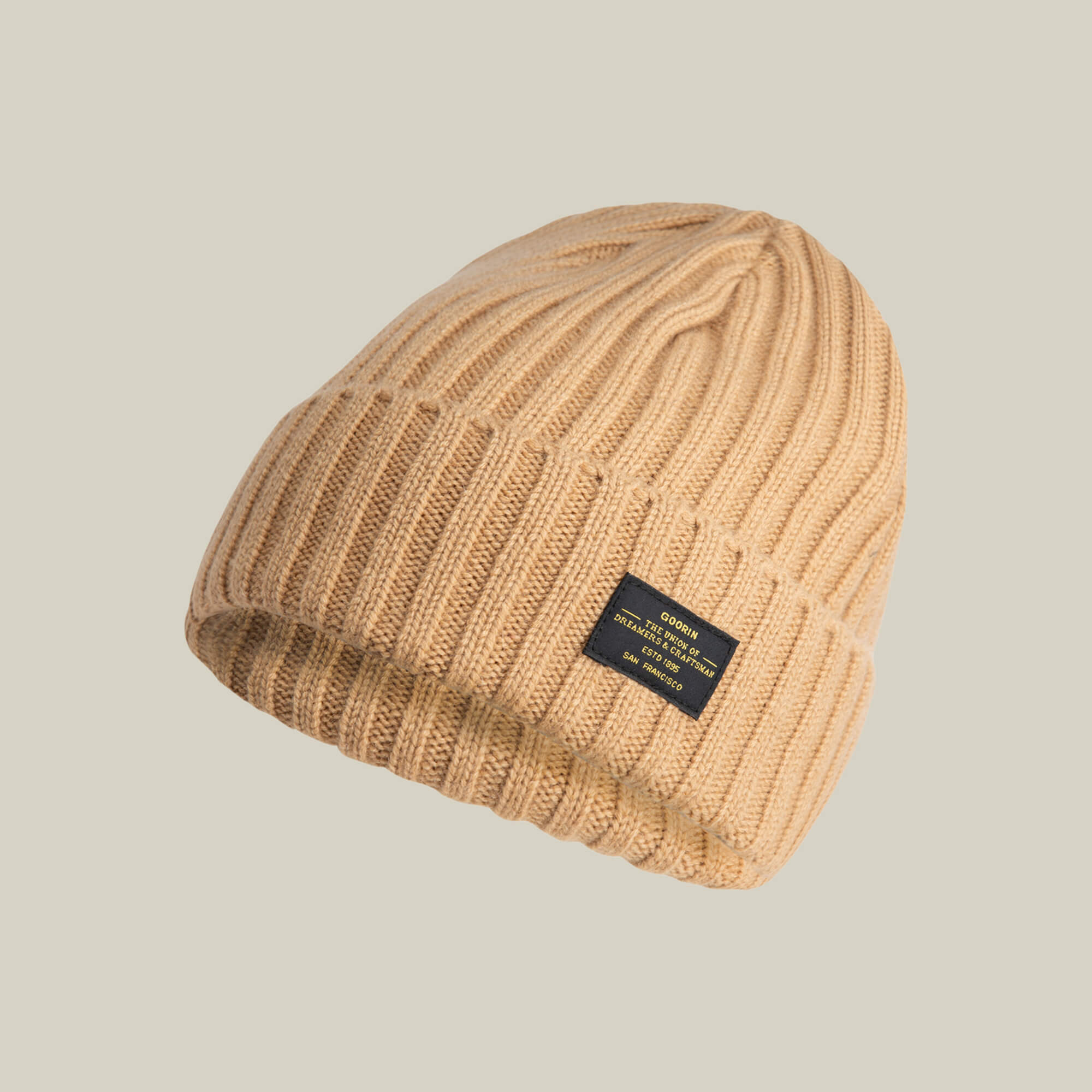 The Dream Cap by Goorin Bros. is a luxurious beige cashmere wool beanie with a ribbed texture, folded brim, and black rectangular front label, shown against a plain light background.