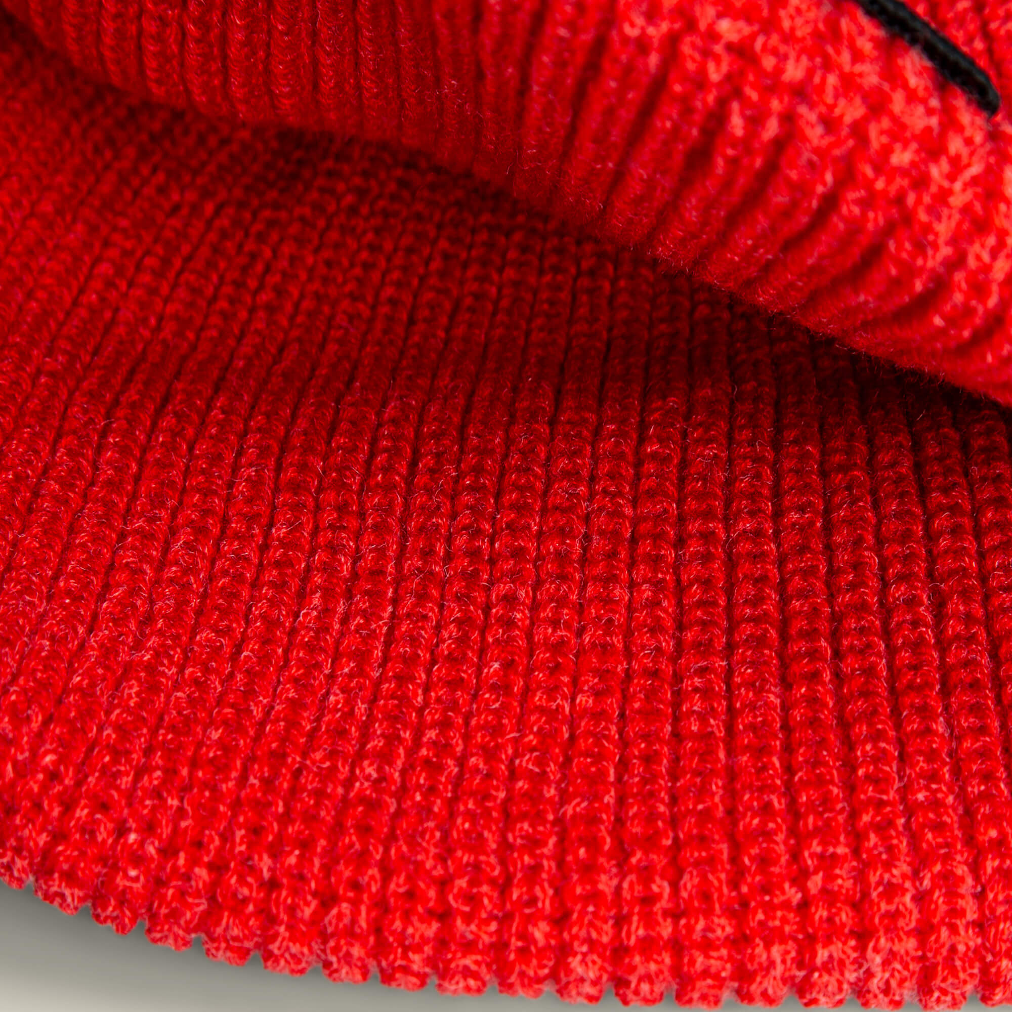 Close-up of The Strength Beanie by Goorin Bros., showcasing its red ribbed knit texture and detailed stitching that evoke rugged warmth.