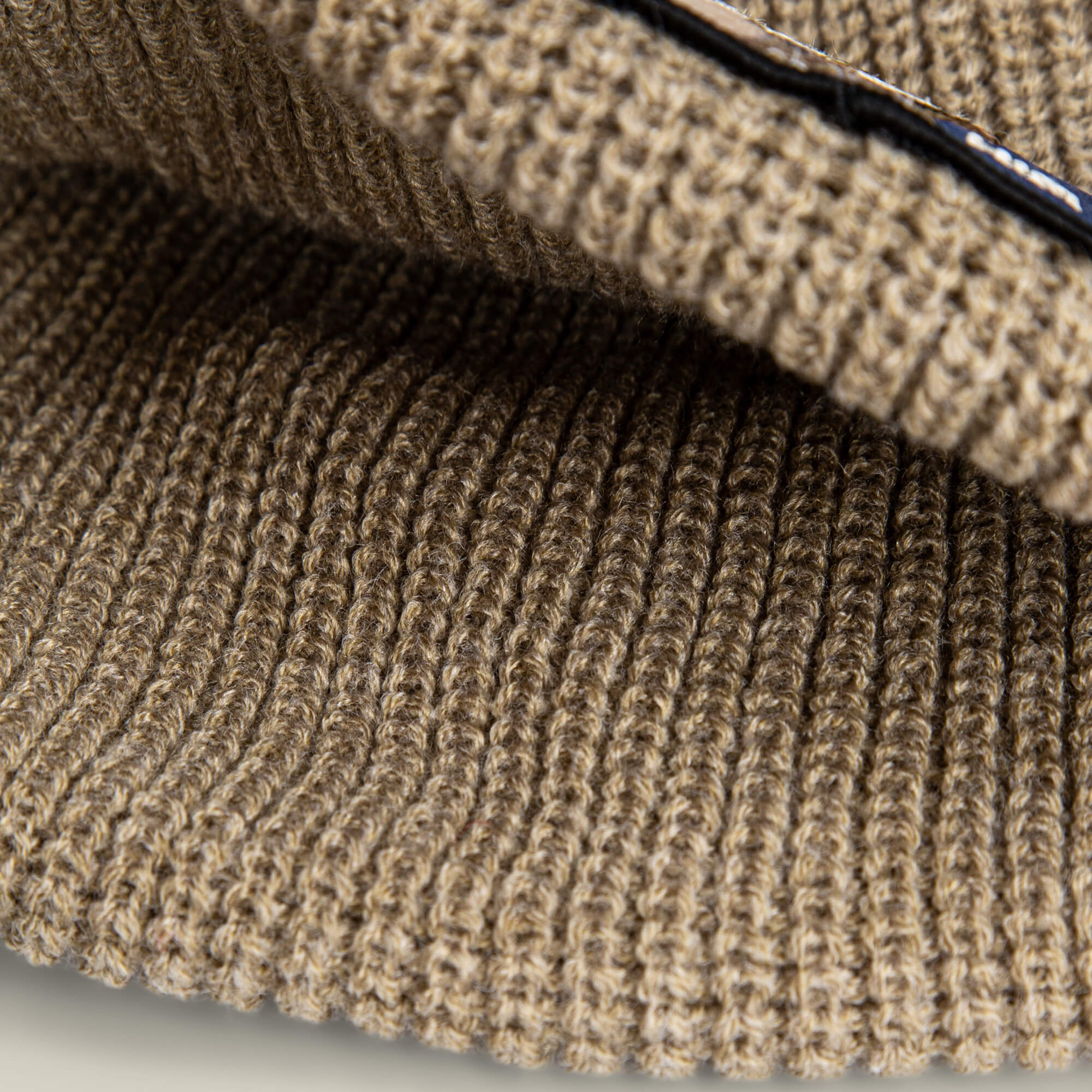 Close-up view of brown ribbed knit fabric with visible stitches, highlighting the cozy texture and details of The Him Beanie by Goorin Bros.—a stylish way to add warmth and flair to your look.