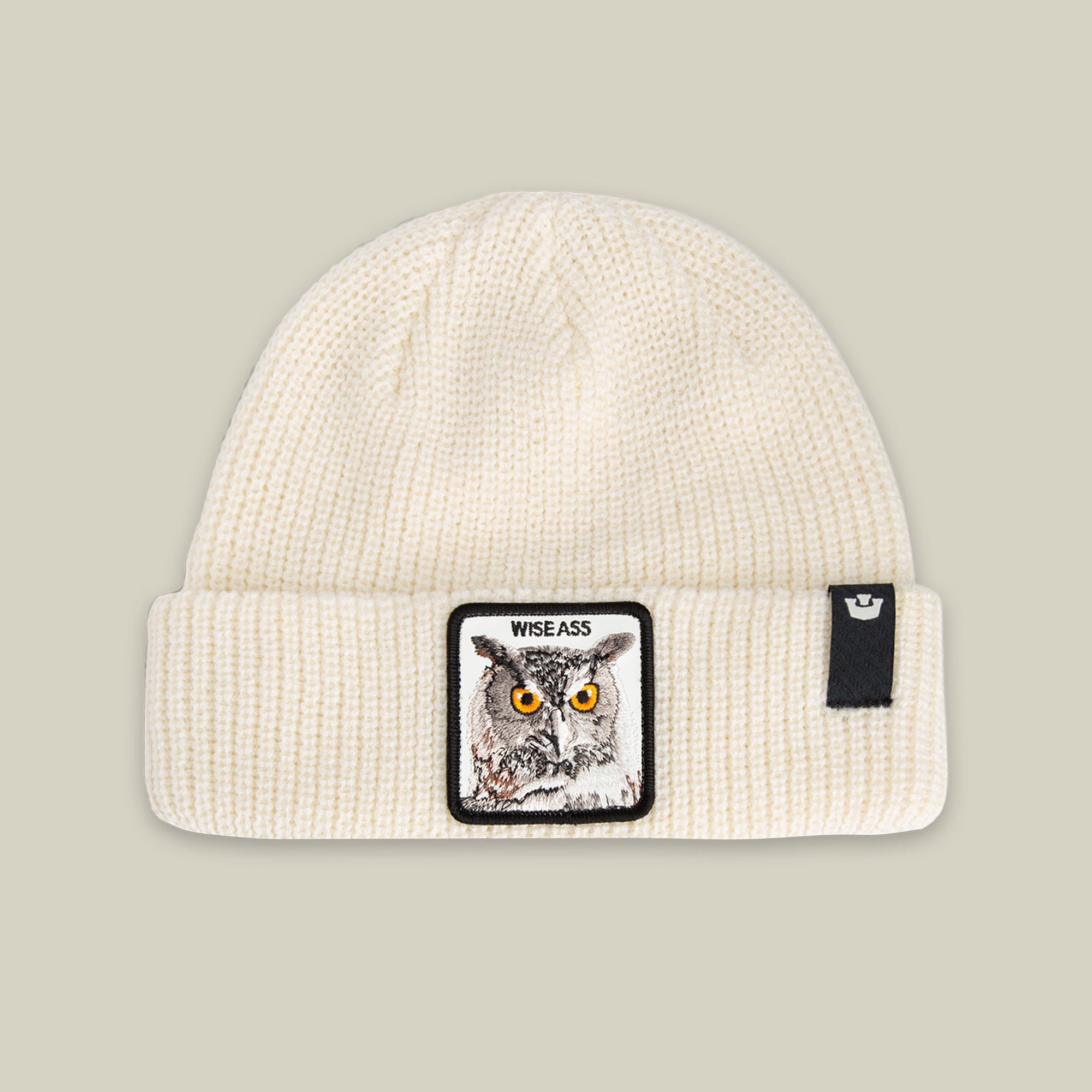 The Wise Ass Beanie by Goorin Bros. in DUST features an owl patch on the front and a small black tag on the cuff.