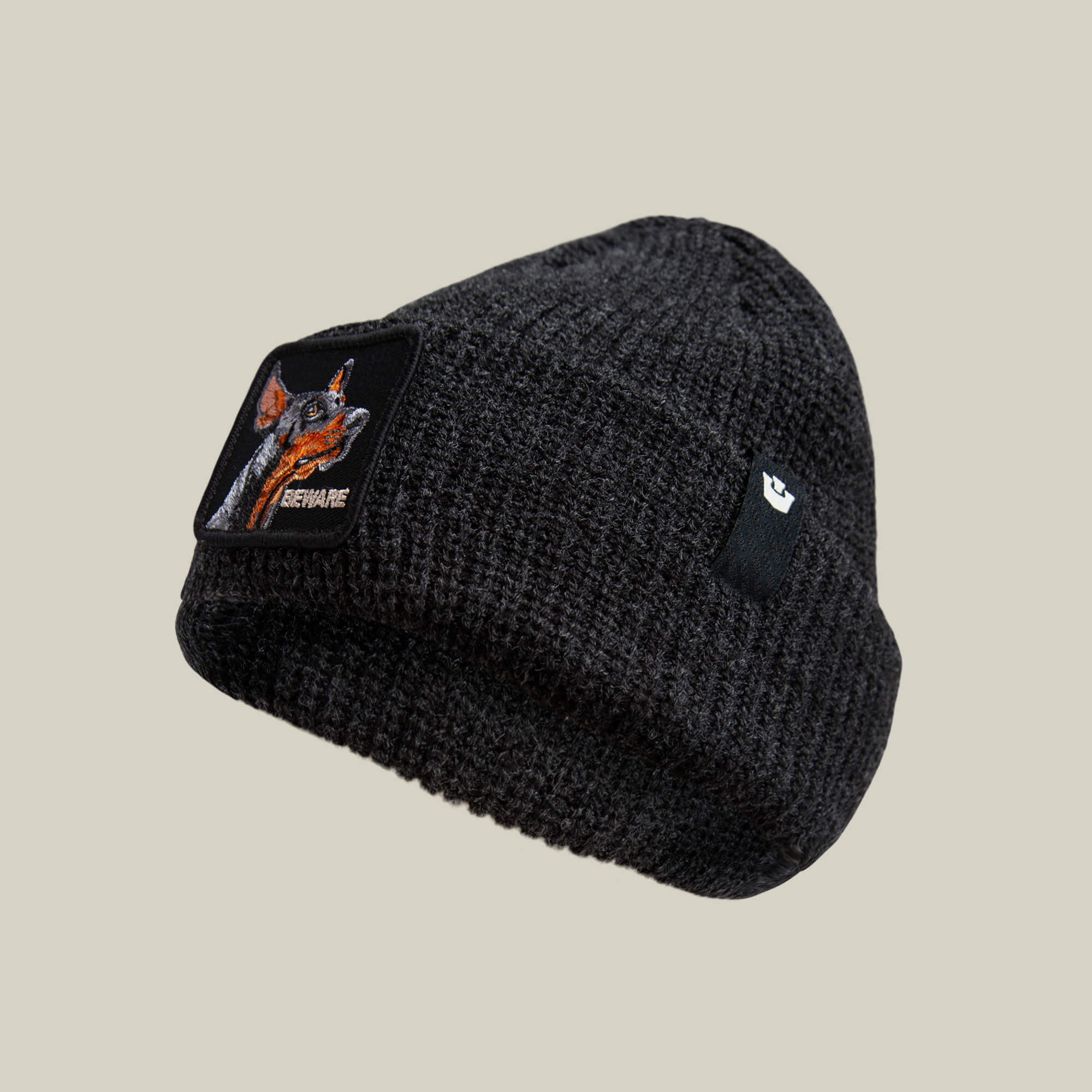 The Beware Dog Beanie by Goorin Bros. is a dark gray heavyweight knit beanie with a dog patch labeled "BEWARE" and a small black cuff tag—perfect for fans of guard dog beanie styles.