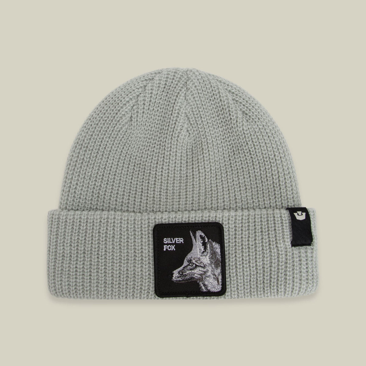 The Silver Beanie by Goorin Bros is a light gray ribbed knit beanie with a black patch featuring a silver fox illustration and text on the front, displayed against a neutral background.