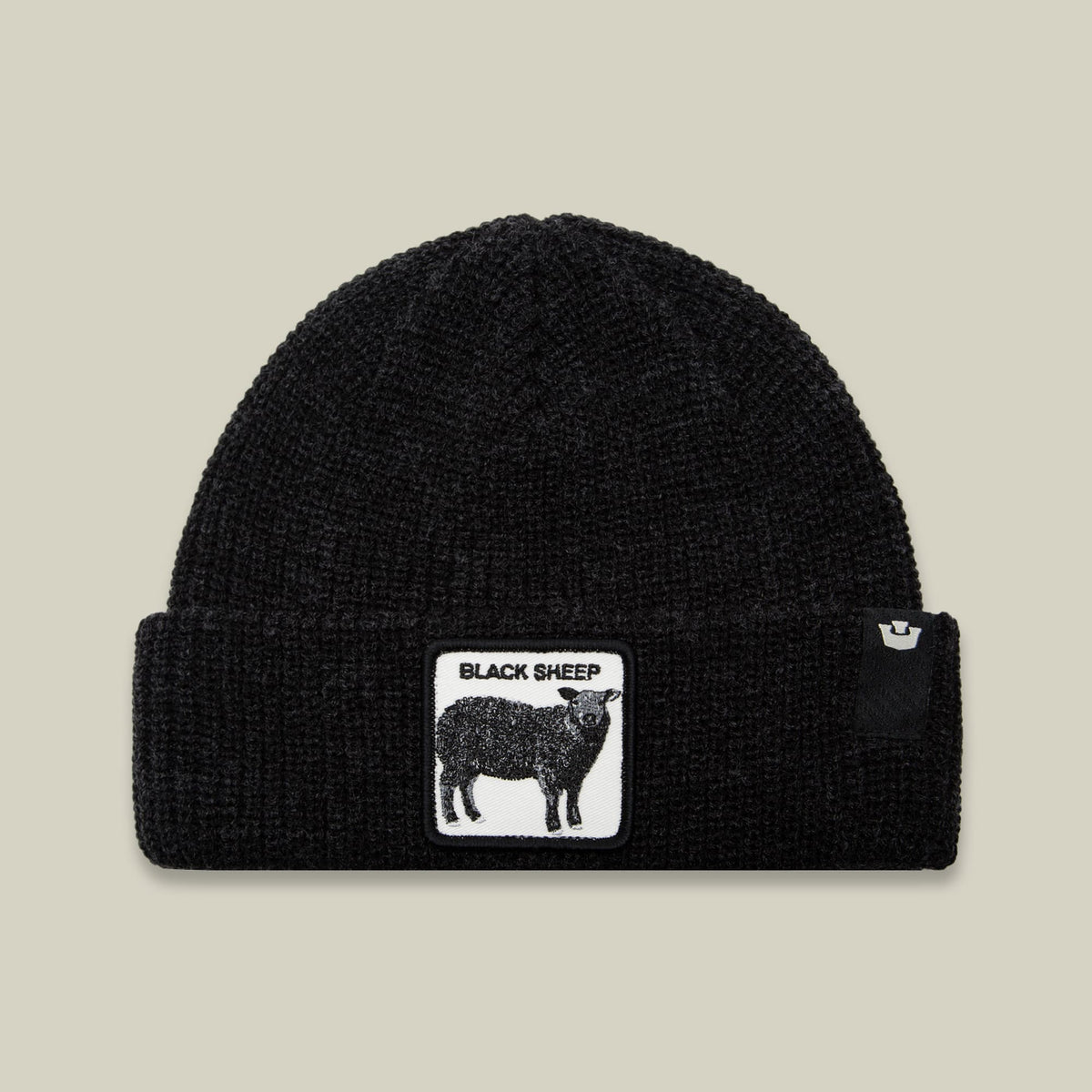 The Black Sheep Beanie by Goorin Bros is a black ribbed knit beanie featuring an embroidered white patch with a black sheep graphic and text on the front, displayed against a neutral background.