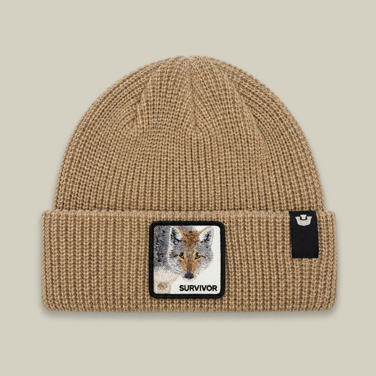 The Survivor Beanie by Goorin Bros is a beige ribbed knit beanie with a wolf head patch featuring embroidery and the word "Survivor" on the front, displayed against a neutral background.