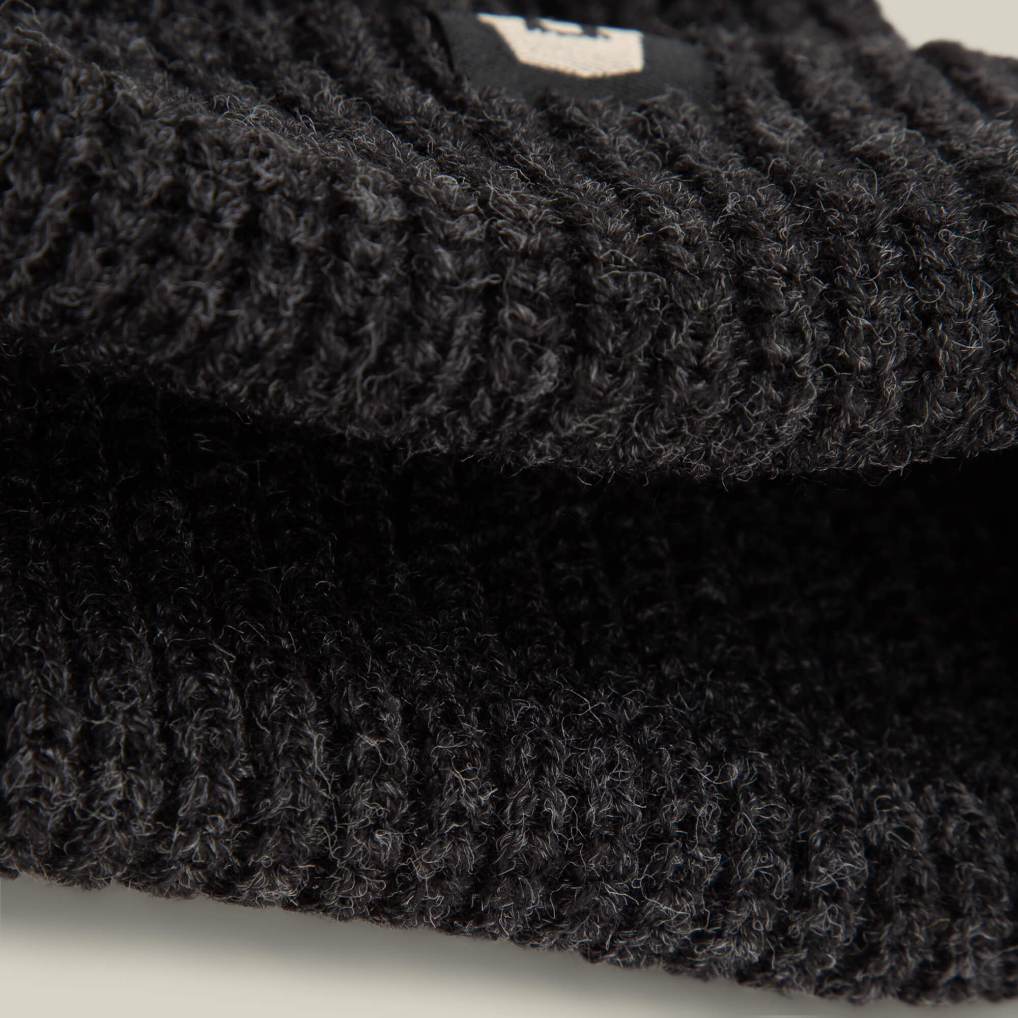 Close-up of black ribbed lightweight poly knit fabric from the Goorin Bros. Air to Fakie, possibly a beanie or sweater, with a small tag partially visible.