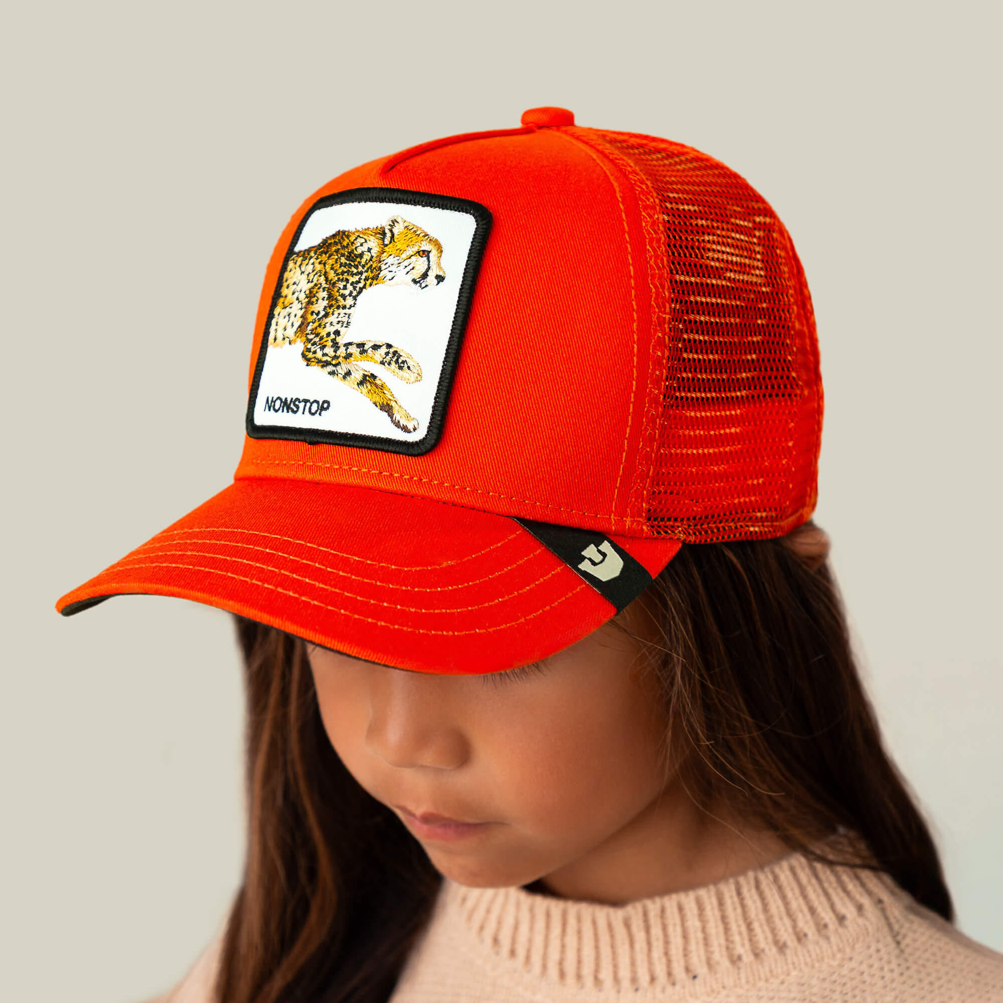 A child wearing The Nonstop Cheetah Mini kids cap by Goorin Bros., featuring an orange crown and a cheetah patch, looks down.