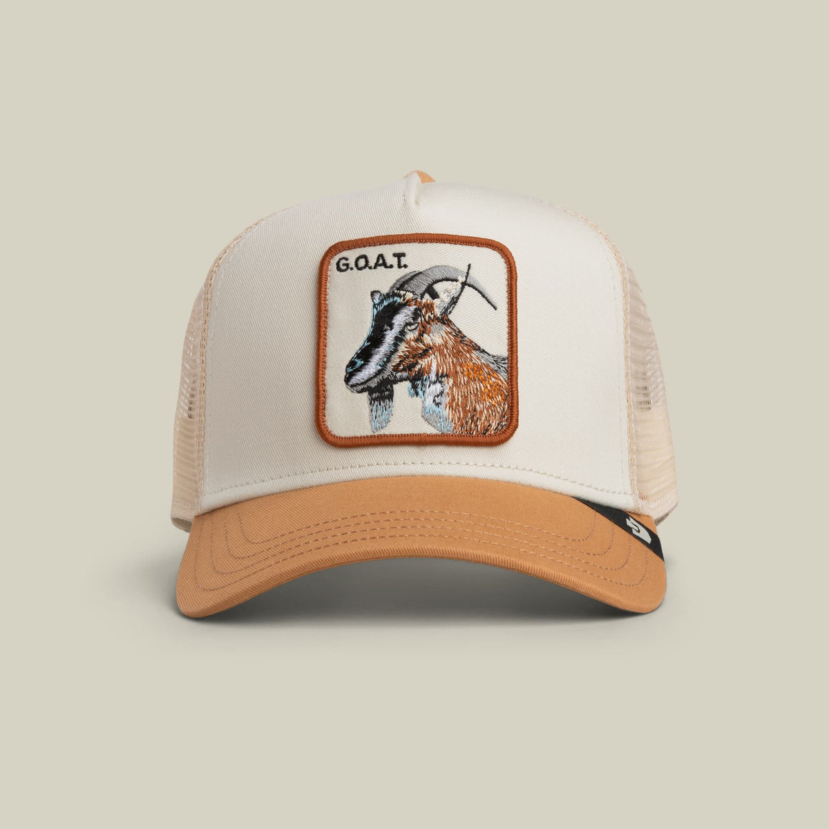 The Goat Trucker Mini by Goorin Bros is a white and tan mesh trucker hat with an orange-bordered patch featuring an embroidered goat head and "G.O.A.T" text, displayed on a neutral background.