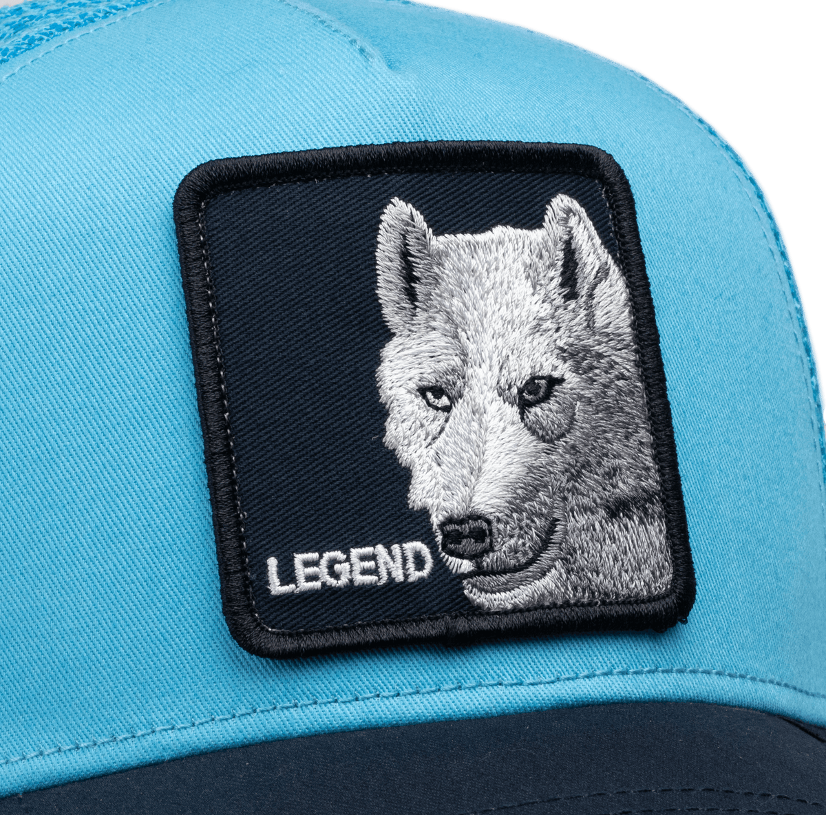 The Goorin Bros. Legend Wolf Trucker Mini is a light blue and black two-tone snapback cap featuring an embroidered white wolf head patch with yellow eyes and the word "Legend" on a dark navy background.