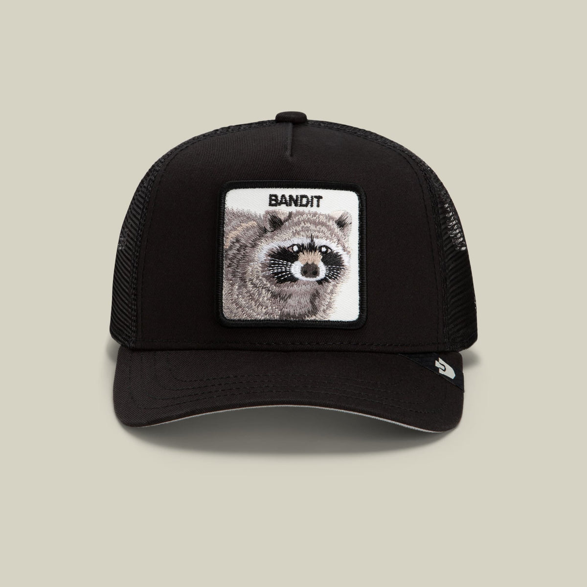 The Goorin Bros. Bandit Trucker Mini is a black mesh snapback cap featuring a white embroidered patch with a detailed raccoon illustration and "BANDIT" text on the front.