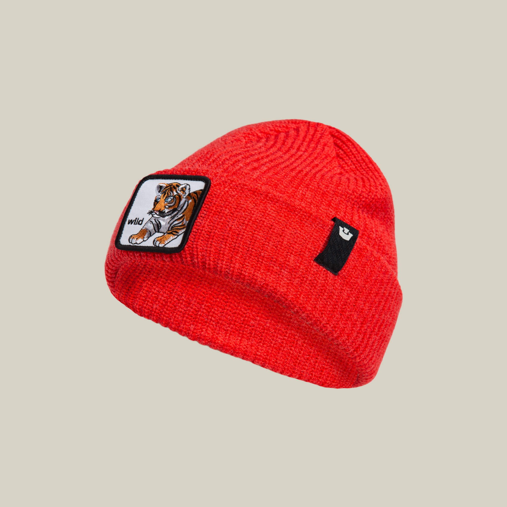 The Goorin Bros. Wild Beanie Mini is a bright red knit beanie for kids, with a rectangular "wild" tiger patch and a small black patch featuring a white symbol.