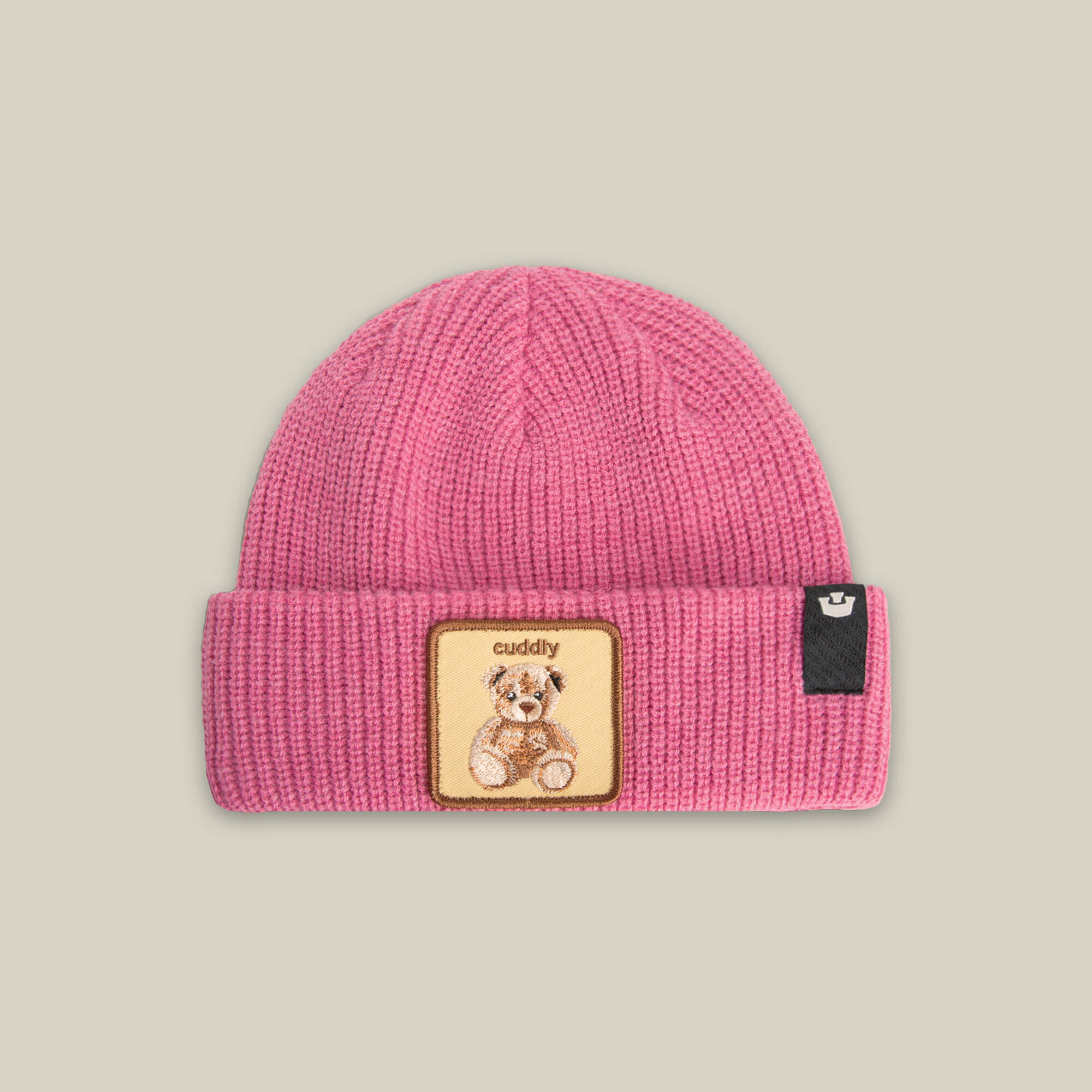 The Cuddly Beanie Mini by Goorin Bros. is a pink soft knit kids beanie with a folded brim, featuring a teddy patch embroidered with "cuddly" and a small black side tag.