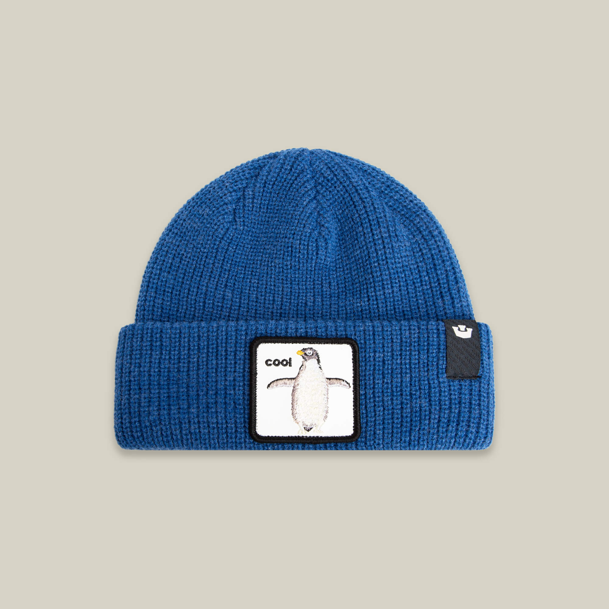 The Penguin Beanie Mini by Goorin Bros. is a blue knit kids hat with a folded brim, featuring a rectangular penguin patch and "cool" text—ideal for adding fun to any snow day.