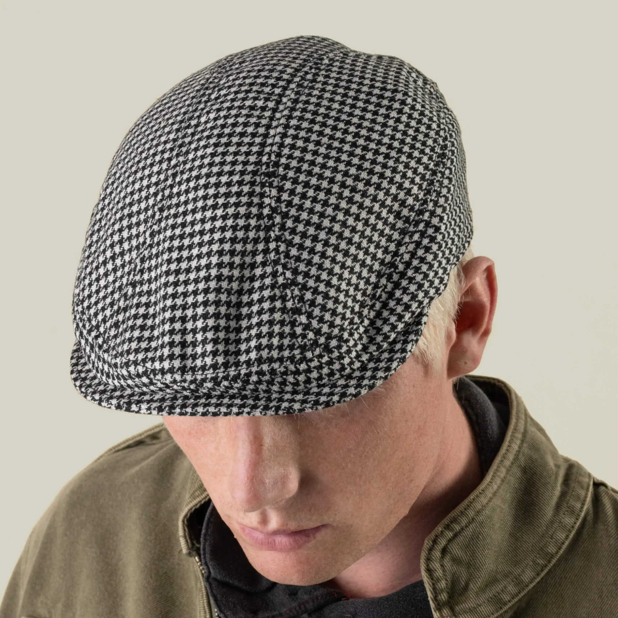 A person wearing the Goorin Bros. “Norwood” black-and-white houndstooth wool flat cap and an olive green jacket, facing downward against a plain background.