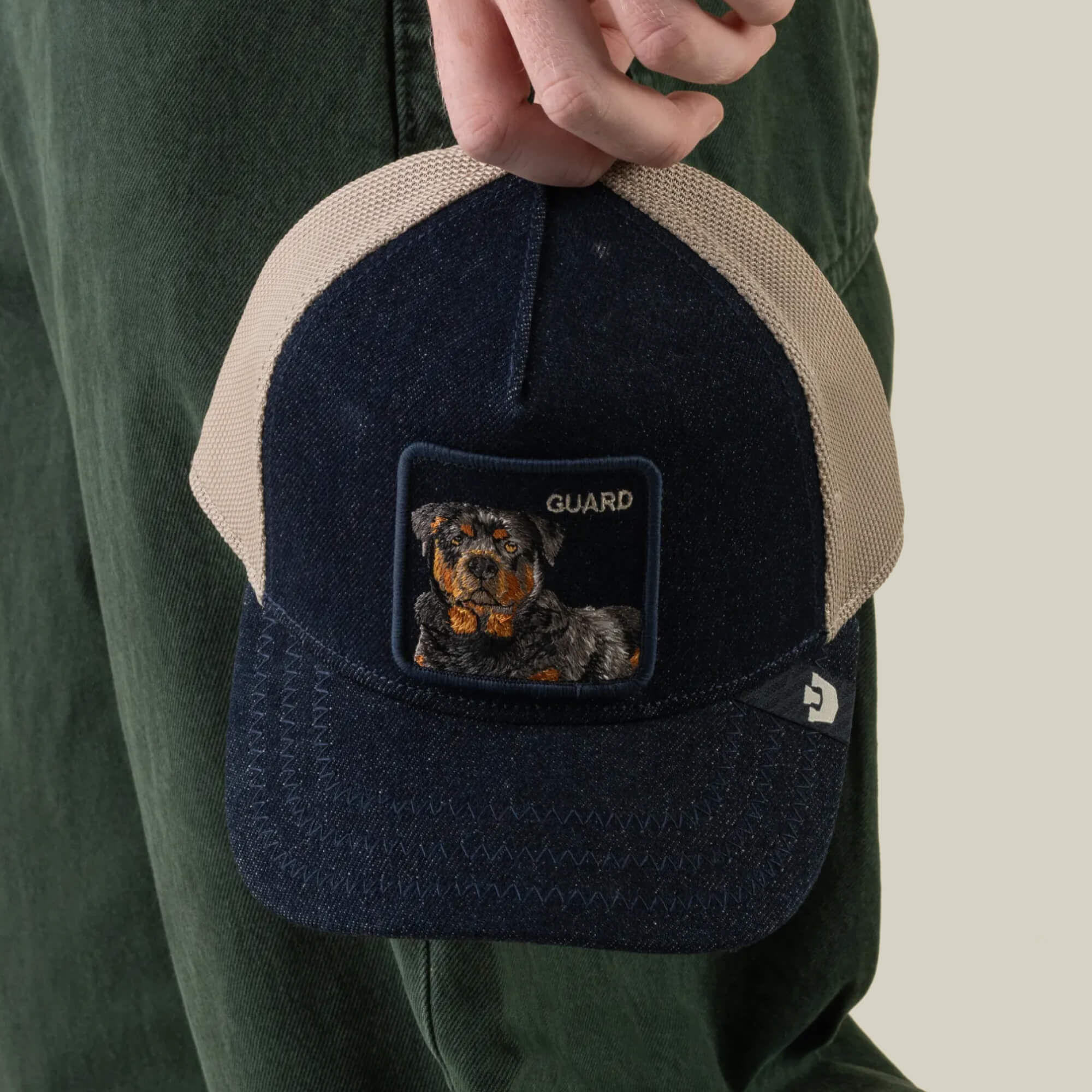 A person holds the Goorin Bros. Denim Guard snapback baseball cap in navy and beige, featuring a patch with an embroidered dog and the word “GUARD.”.