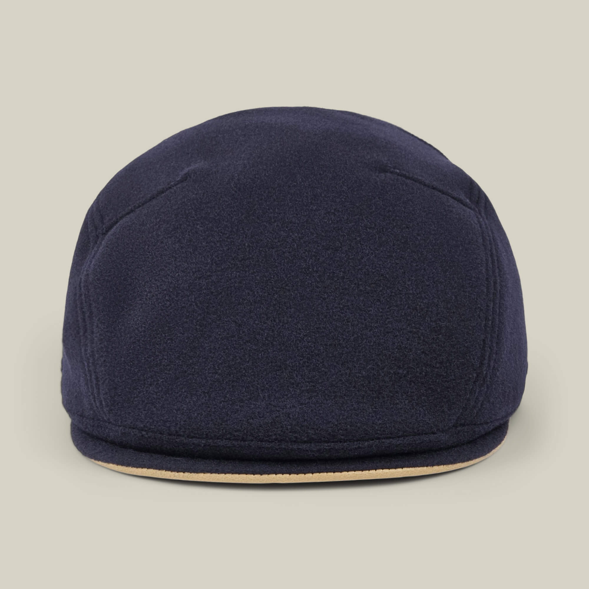 The Cornerstone flat cap by Goorin Bros.—a navy blue wool design, handmade in New Jersey with a round crown and short, curved brim—is photographed against a plain beige background.