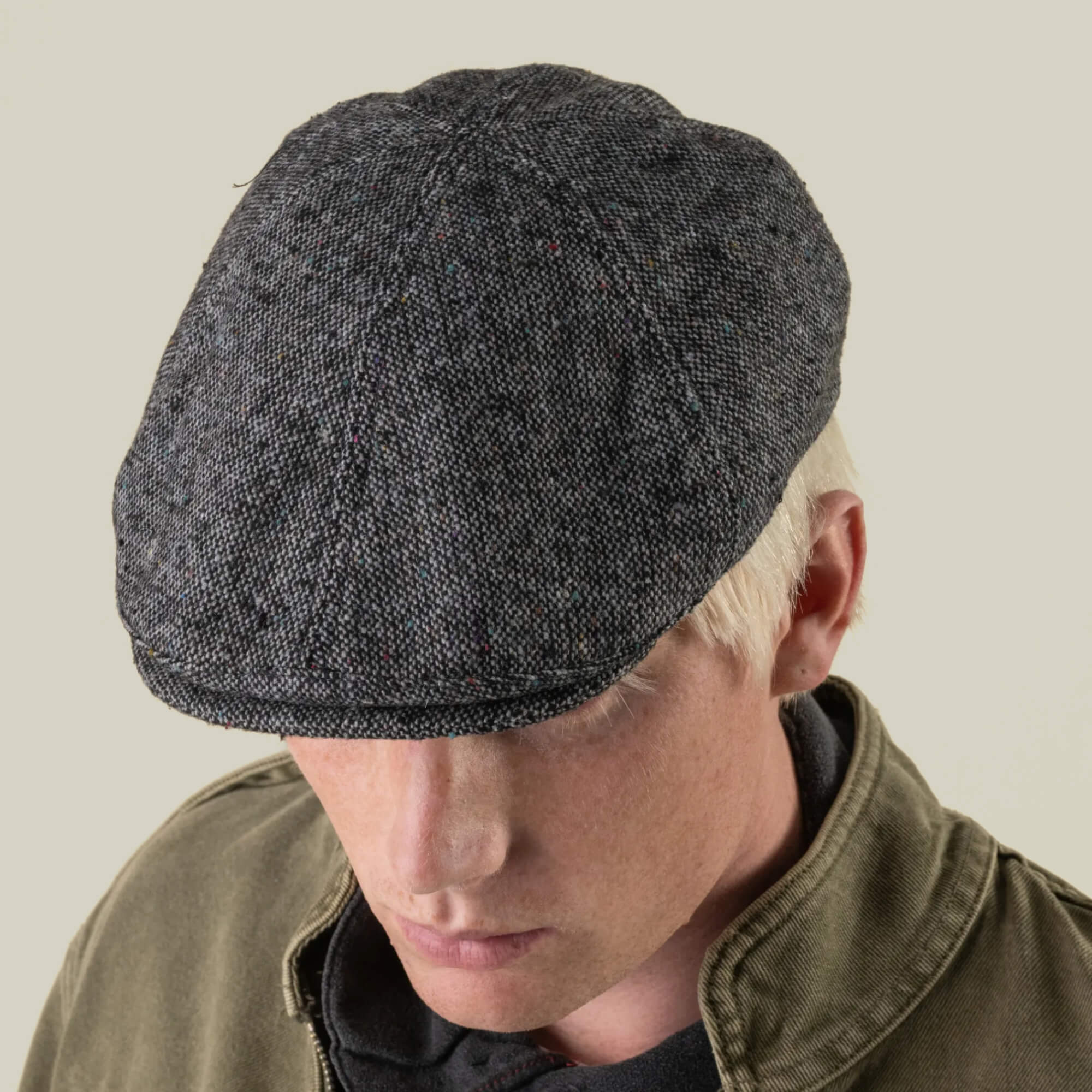 A person with light hair wears the Goorin Bros. Newlands flat cap in digital gray and a dark olive green jacket, looking downward against a plain background.