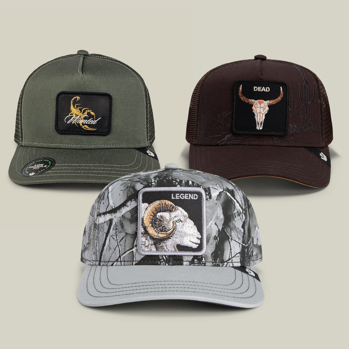 Three trucker hats from the Goorin Bros. Low Pro Bundle are displayed: an olive “Scorpion” hat with an eagle patch, a brown option featuring a maroon “Longhorn Skull DEAD” patch, and a legend grey camo hat with a “Ram LEGEND” patch.