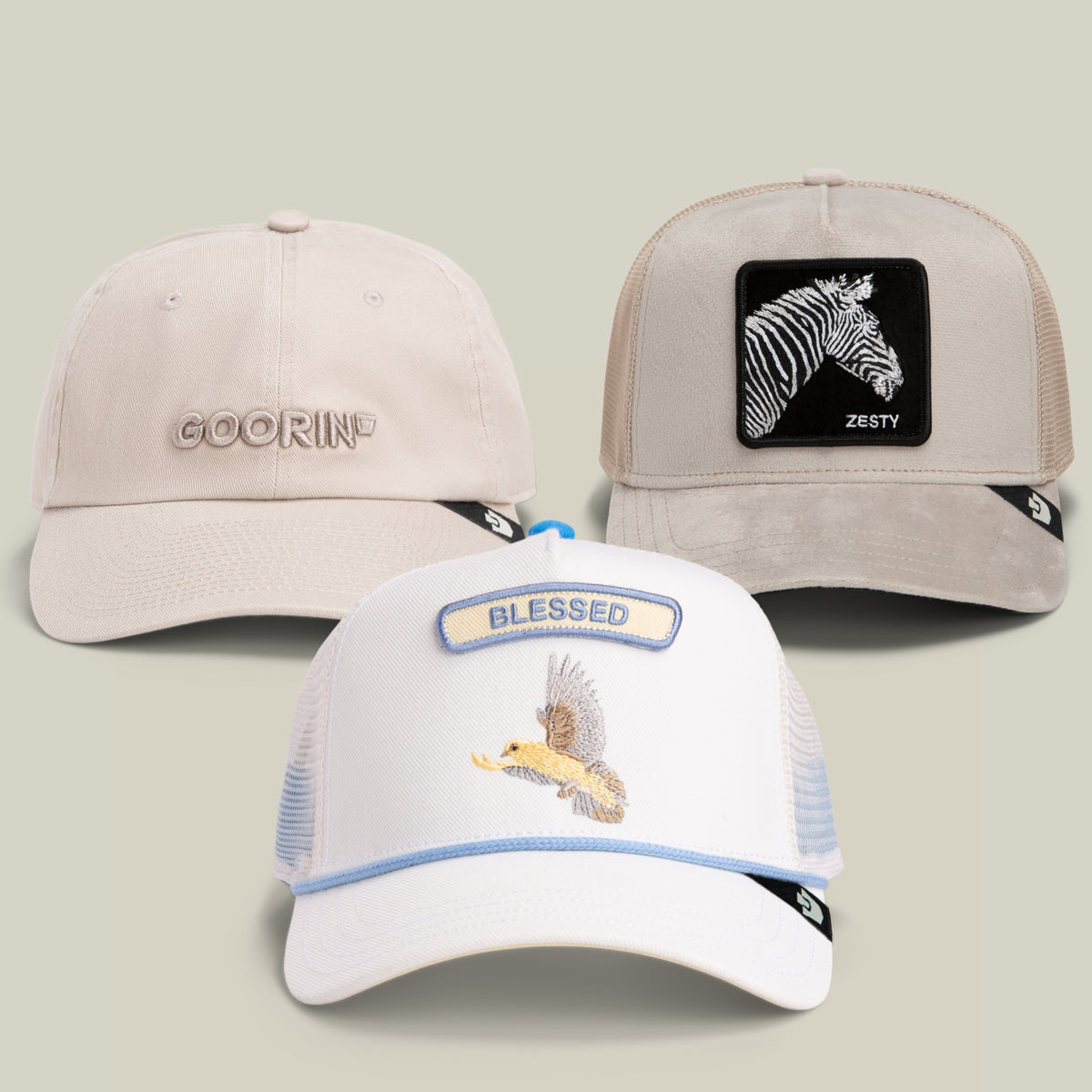 The Mr. Brightside Bundle by Goorin Bros. showcases three baseball caps: a cream dad cap with the GOORIN logo, a gray cap featuring a tan zebra patch labeled “ZESTY,” and a white eagle cap embroidered with the word “BLESSED.”.