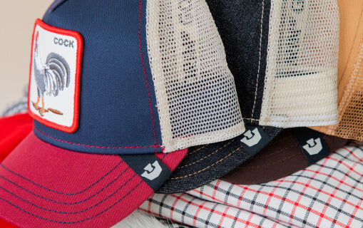 A close-up view of several trucker hats stacked together, featuring mesh panels and a patch with a rooster on the front cap—showcasing bold hat designs perfect for standing out.