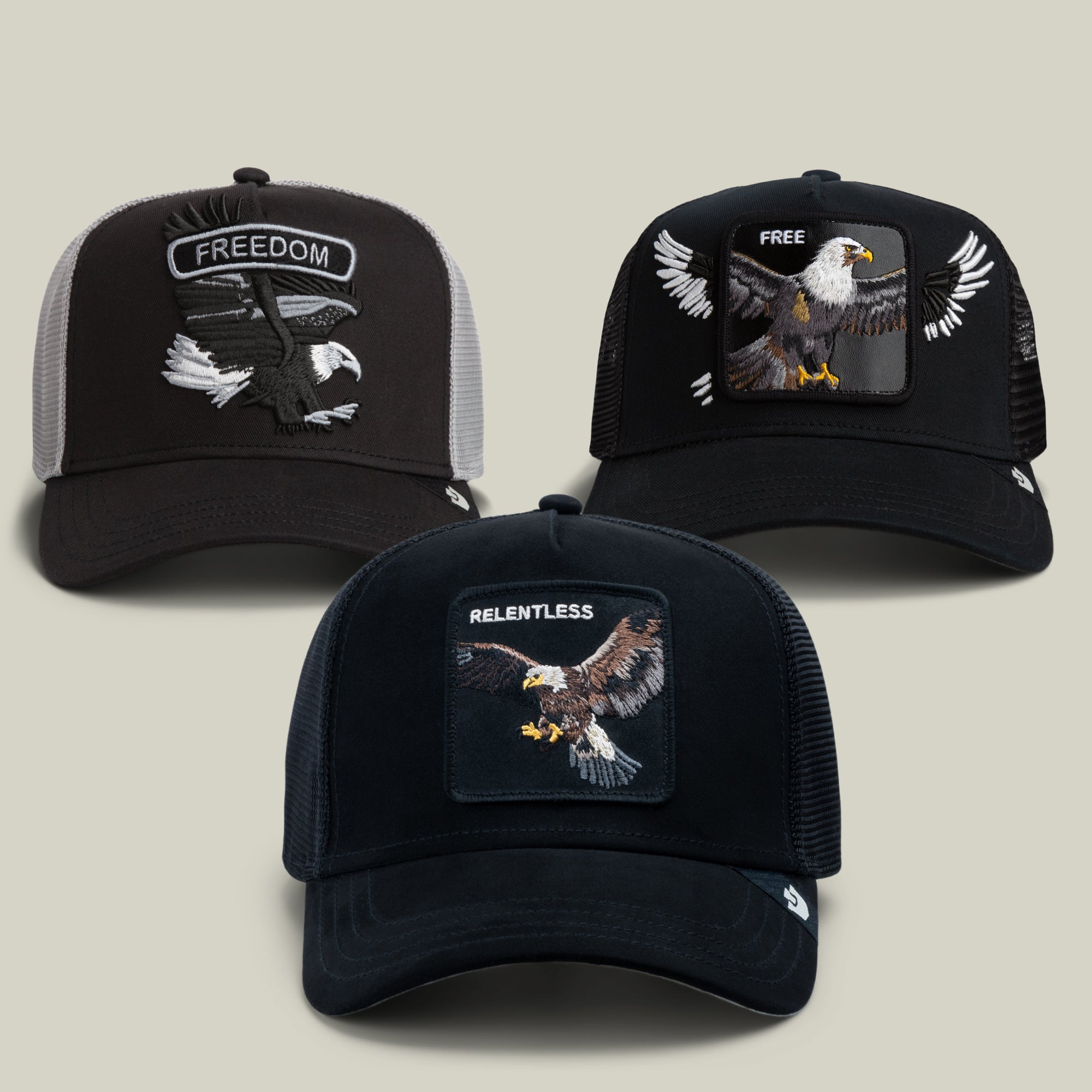 The Take Flight Bundle by Goorin Bros. includes three eagle caps featuring dramatic birds of prey graphics and bold lettering: FREEDOM on black and gray, FREE on black, and RELENTLESS on dark blue; each hat comes with a mesh back and a curved brim.