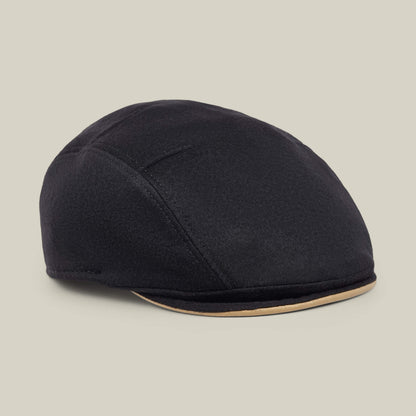 The Goorin Bros. “Cornerstone” is a black wool flat cap, handmade in New Jersey, featuring subtle stitched details and a contrasting beige trim along the brim, displayed on a neutral background.
